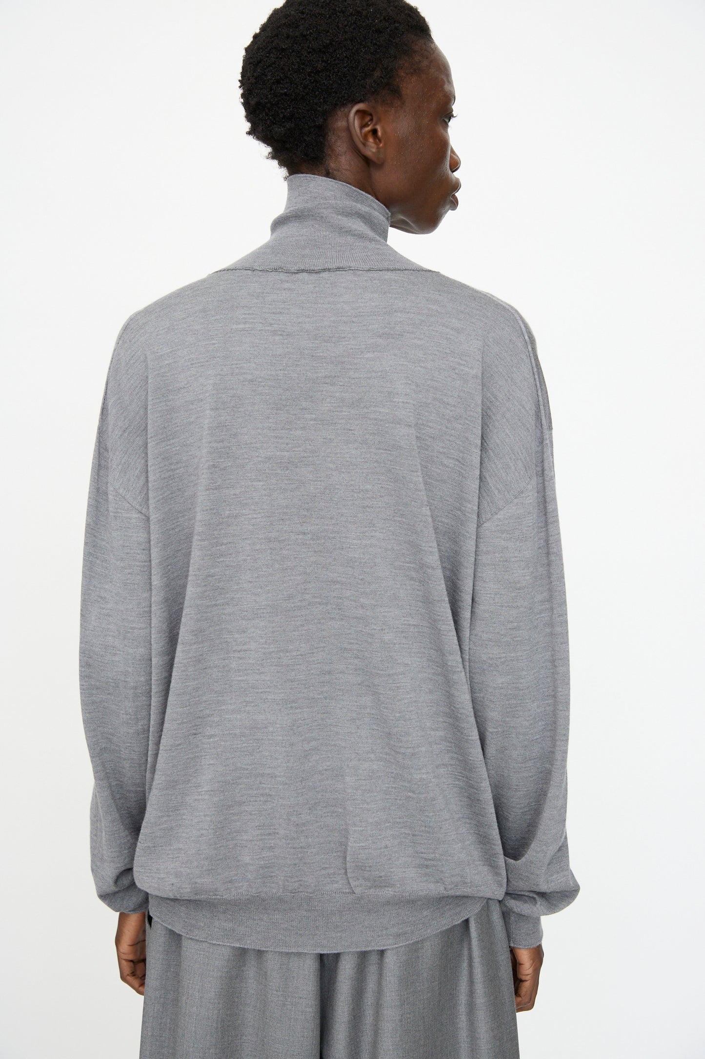 Model shown from the back wearing Sofie D'Hoore's Merino Maffei Sweater in Steel Melange with gray pants, set against a plain white background.