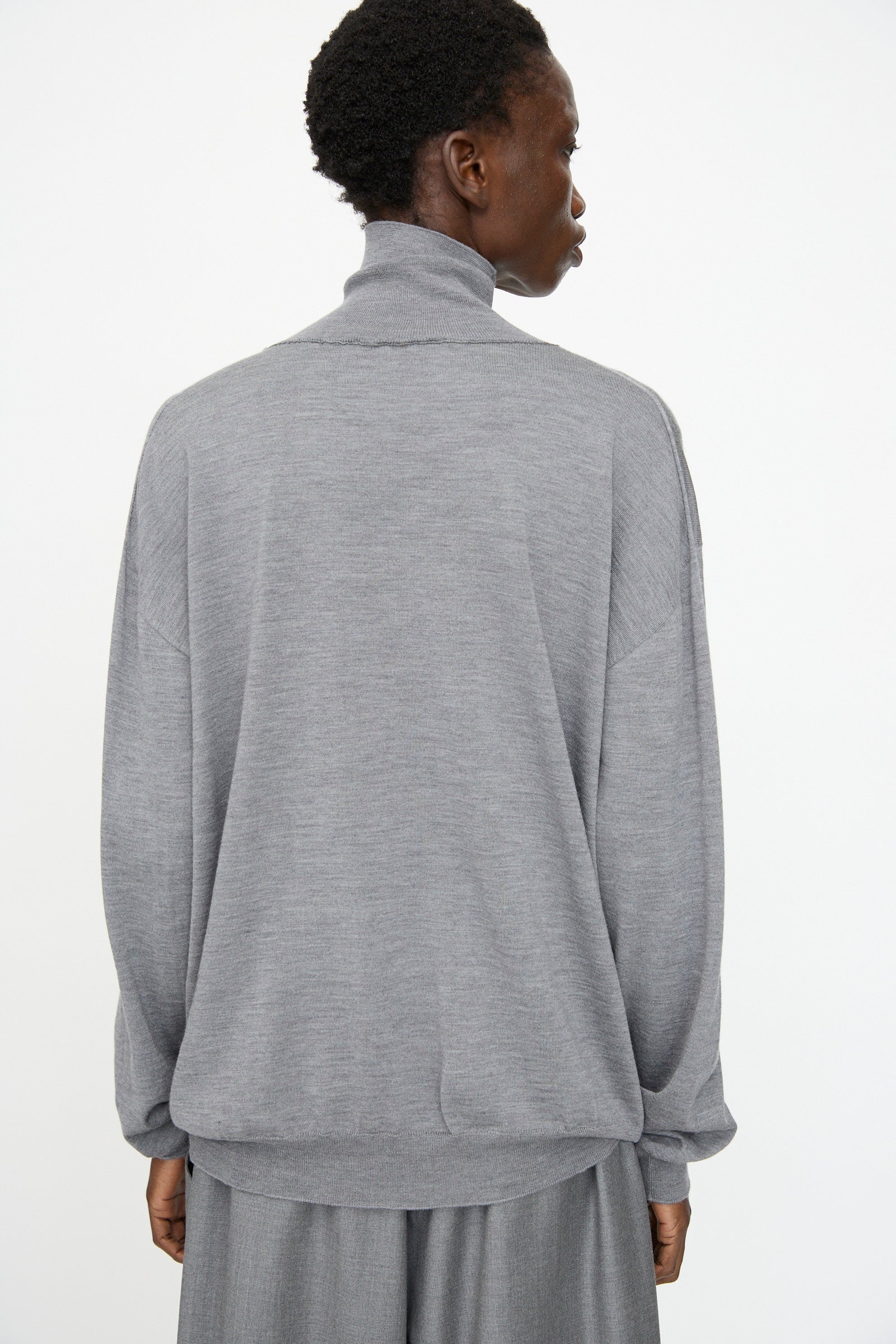 Model shown from the back wearing Sofie D'Hoore's Merino Maffei Sweater in Steel Melange with gray pants, set against a plain white background.