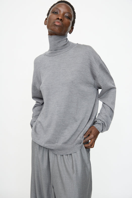 A person in the Sofie D'Hoore Merino Maffei Sweater in Steel Melange and matching gray pants stands against a plain white background.