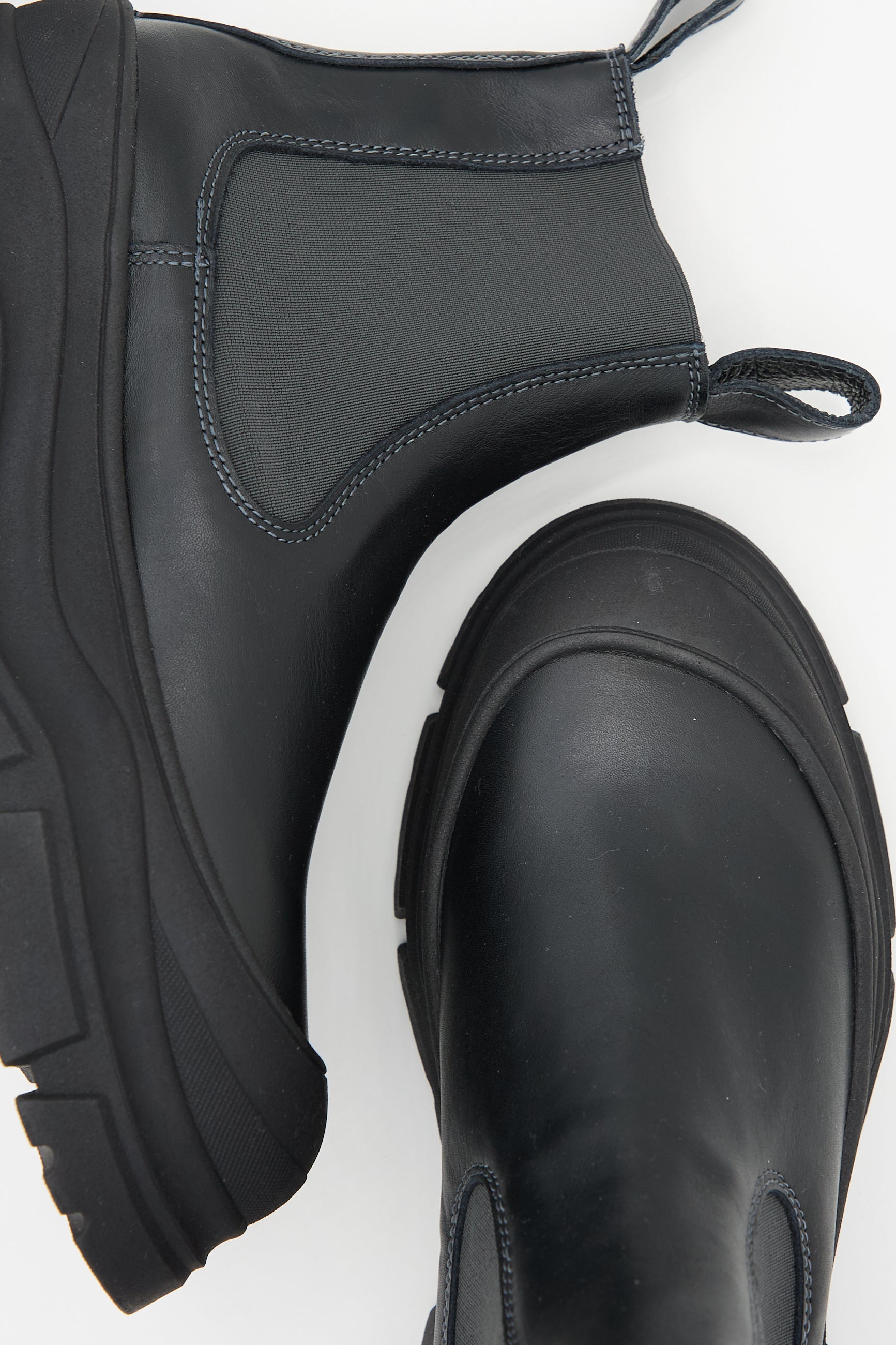 A pair of Sofie D'Hoore's Nappa Leather Fabulous Boots in Black, showcasing elastic side panels and convenient pull tabs. One boot is displayed from the side, highlighting its sleek design, while the other is presented from above, emphasizing the sophisticated rubber cap toe.