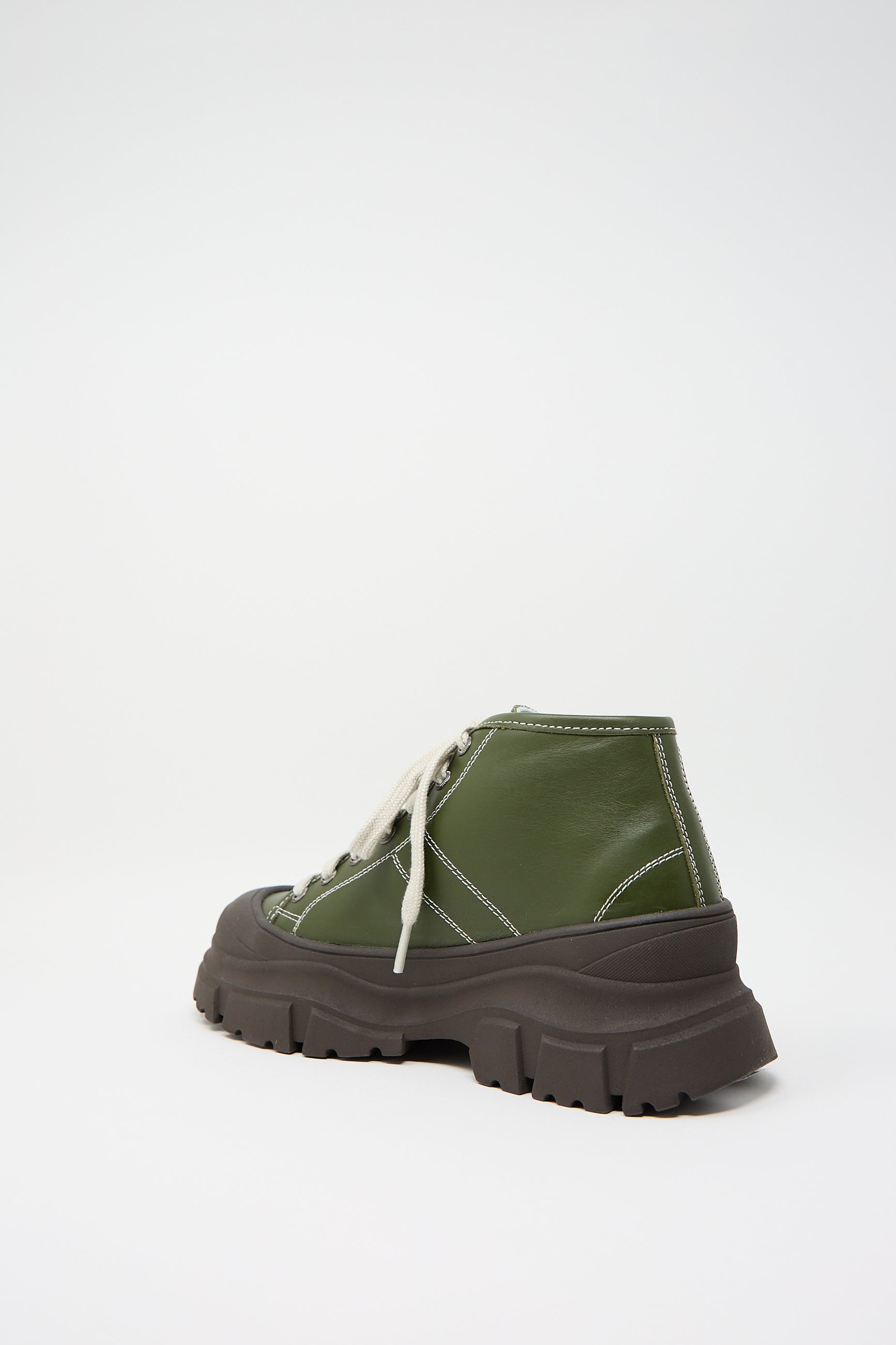 A green high-top Nappa Leather Fairway Sneaker in Forest by Sofie D'Hoore, featuring thick grooved black soles, a rubber cap toe, and white laces, displayed against a plain white background.