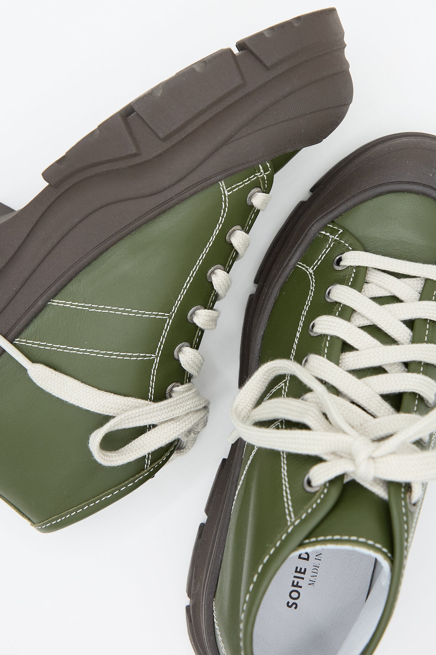 A pair of Nappa Leather Fairway Sneakers in Forest by Sofie D'Hoore with thick black soles and white laces, partially overlapping against a plain white background.