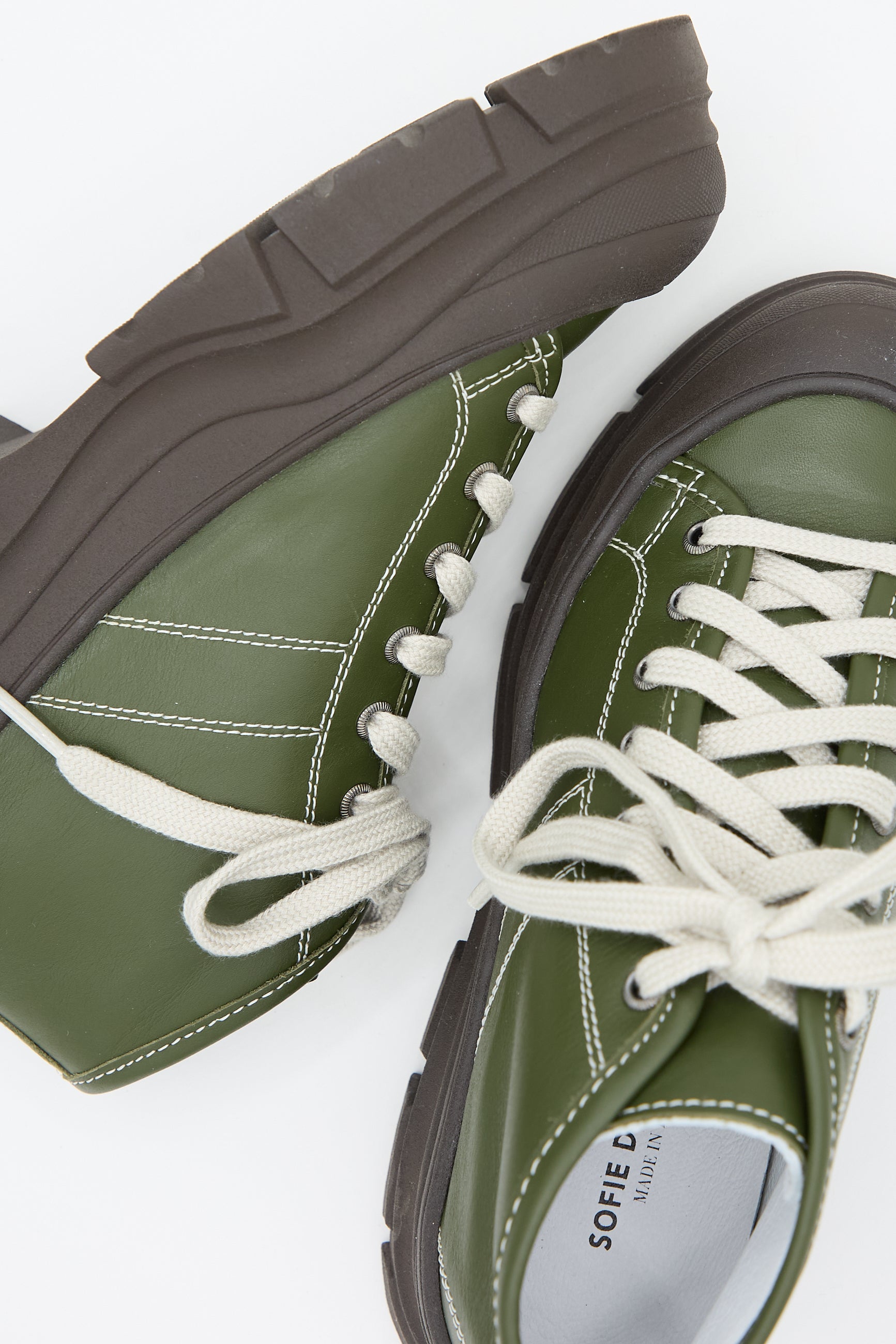 A pair of Nappa Leather Fairway Sneakers in Forest by Sofie D'Hoore with thick black soles and white laces, partially overlapping against a plain white background.