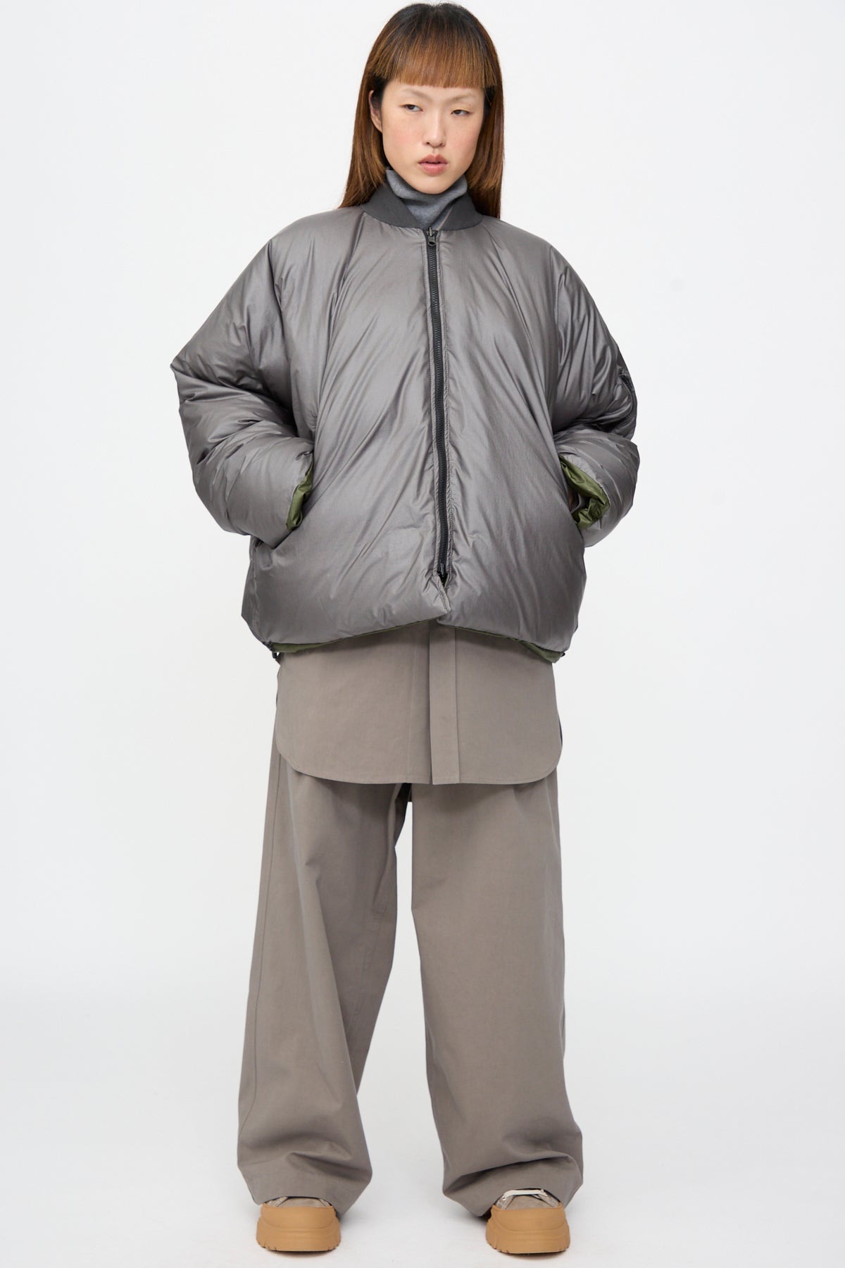 Sofie D’Hoore Origin Down Jacket in Charcoal and Khaki, an oversized, reversible puffer with a khaki green lining, paired with wide-leg khaki trousers and tan platform shoes.