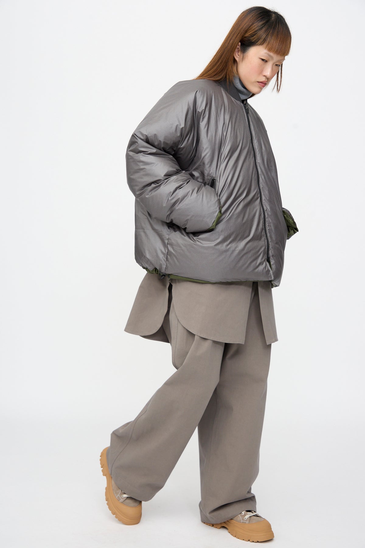 A person wearing a Sofie D’Hoore Origin Down Jacket in Charcoal and Khaki over taupe wide-leg trousers and tan lug-sole shoes.