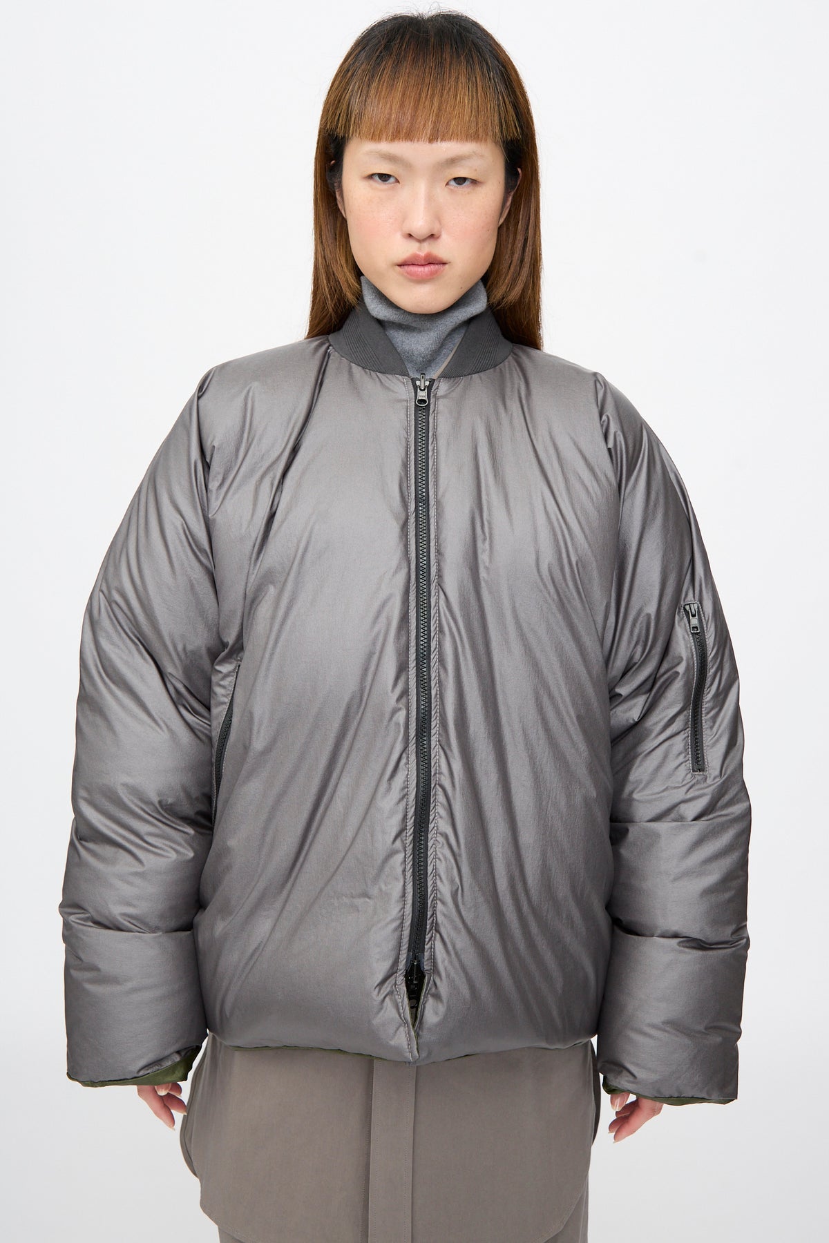 A person wears an oversized, charcoal-colored, zip-front Sofie D’Hoore Origin Down Jacket in Charcoal and Khaki.