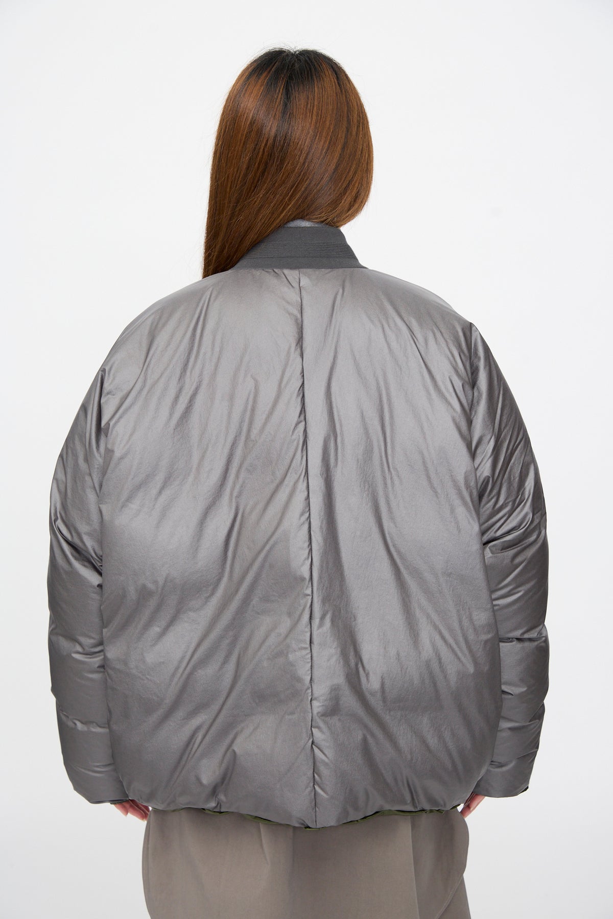 Back view of a charcoal and khaki Sofie D’Hoore Origin Down Jacket, an oversized reversible puffer worn over khaki trousers.