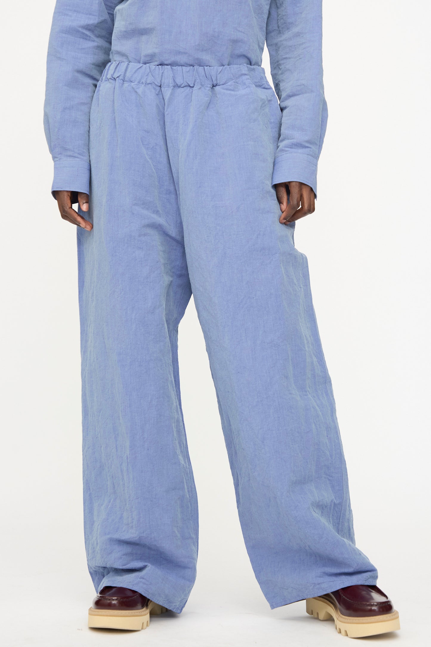 A person wears the Sofie D'Hoore Pavon Pant in Blue Jean with a matching long-sleeve top and burgundy platform shoes, standing against a plain background.