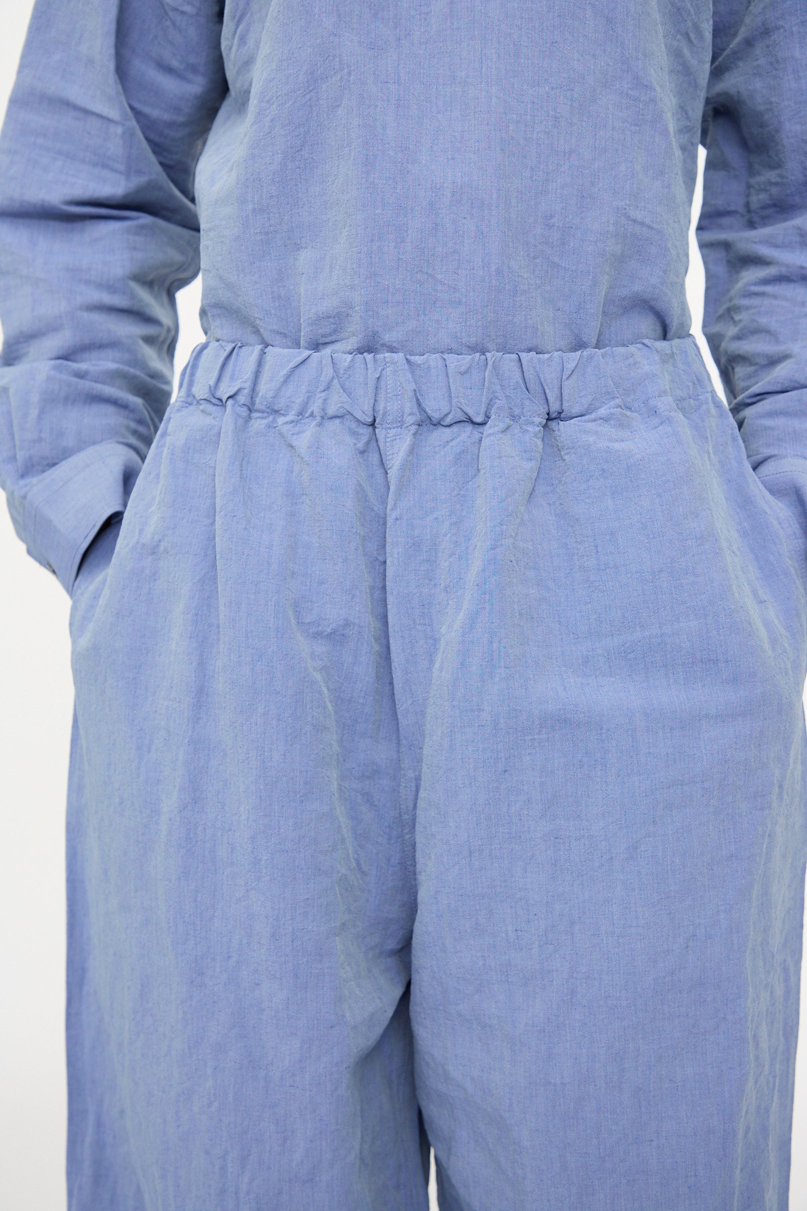 A person wears the Sofie D'Hoore Pavon Pant in Blue Jean, with hands in pockets; image focuses on torso and waist, highlighting the oversized linen pants with an elastic waistband.