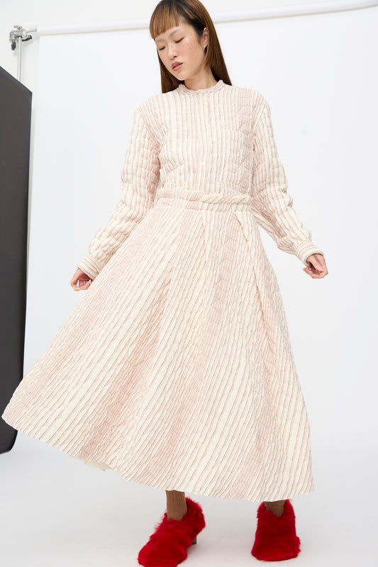 A person wearing a long-sleeved quilted Quilted Cotton Savy Skirt in Red Stripe midi dress with thin red stripes and bright red fuzzy shoes.