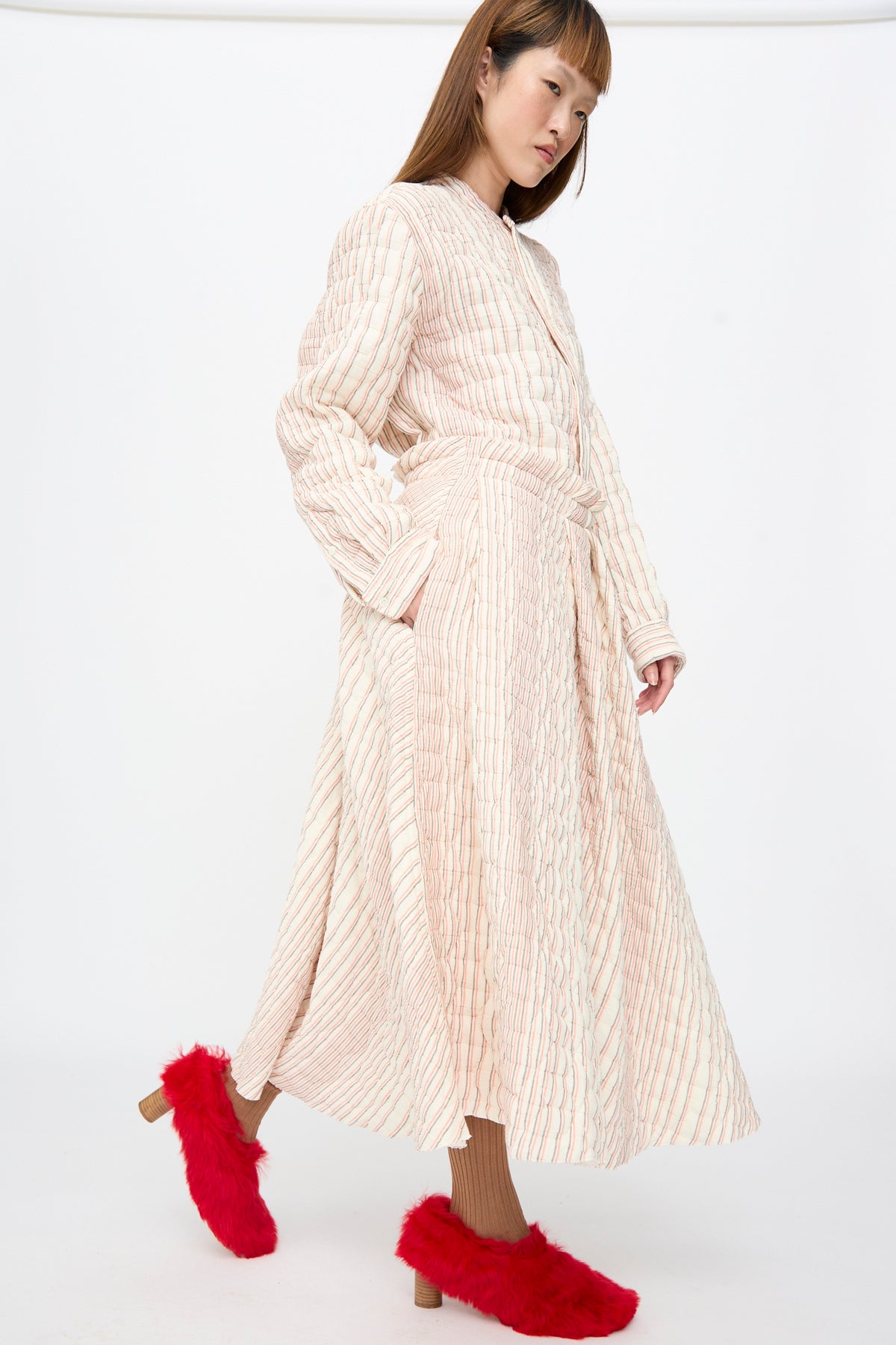 A person wearing a long-sleeved, quilted Quilted Cotton Savy Skirt in Red Stripe midi dress with an A-line skirt and bright red faux-fur heeled shoes.