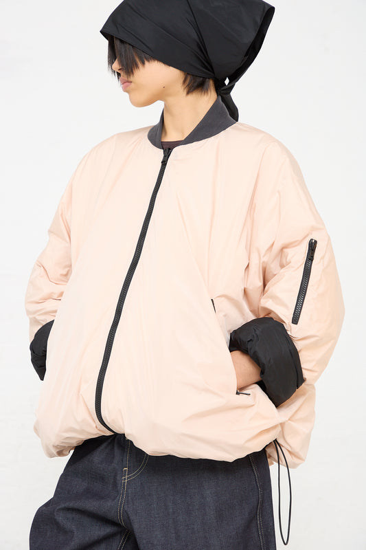 A woman wearing a pink Sofie D'Hoore Quilted Down Reversible Orion Bomber jacket and black hat.