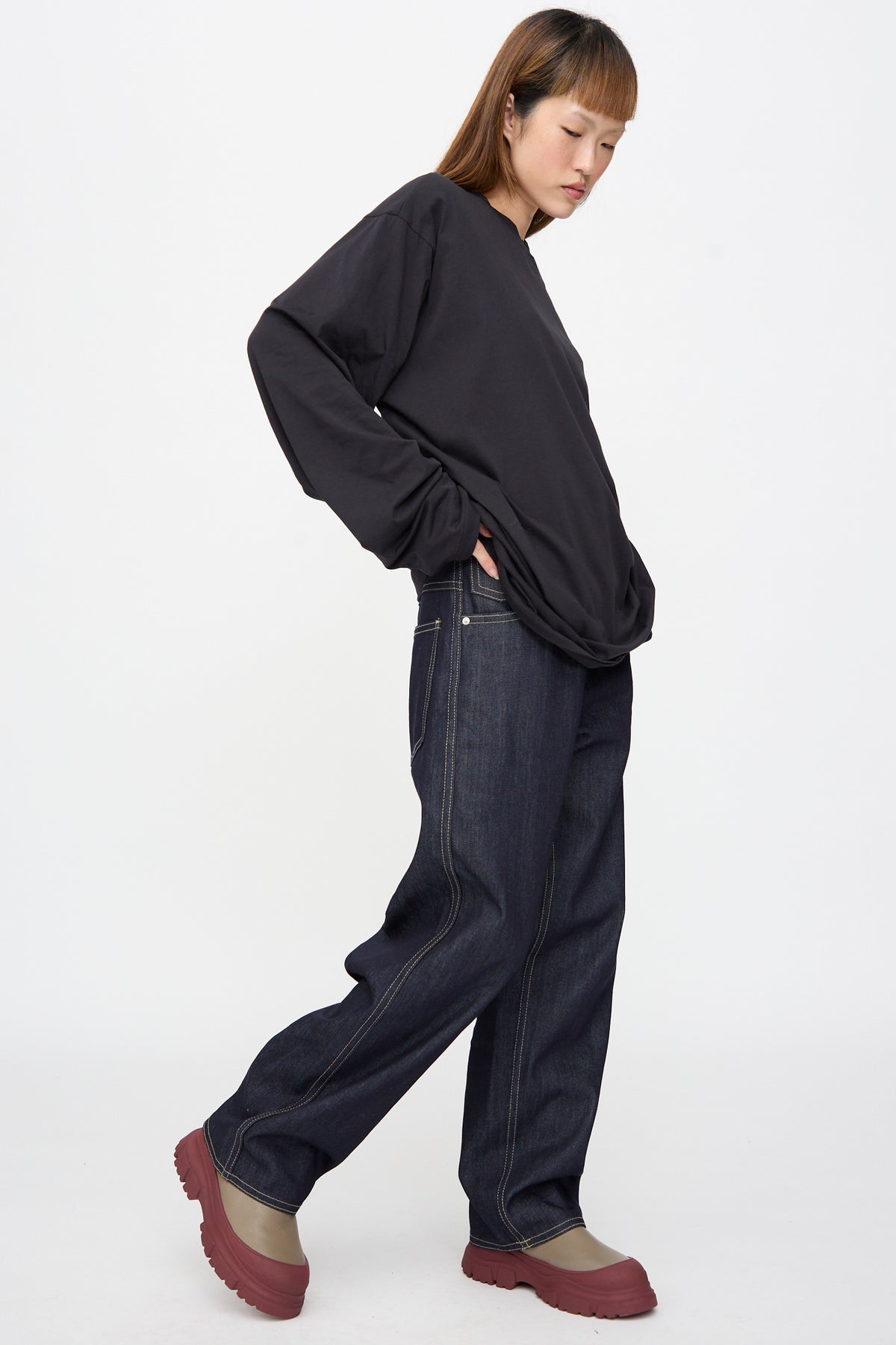 A person wears a black long-sleeve shirt, Sofie D’Hoore Raw Denim Phill Pant in Midnight with contrast stitching, and red-soled boots.