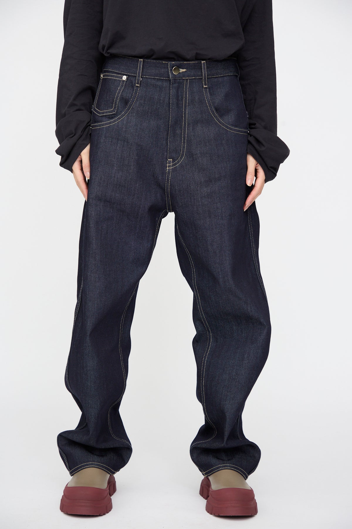Dark indigo Raw Denim Phill Pant in Midnight with contrast stitching, worn with a black long-sleeved shirt and chunky platform shoes.