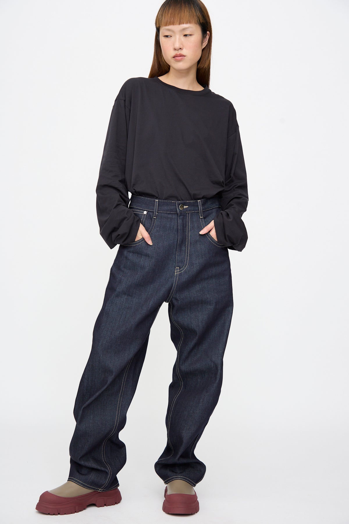 A person wearing a black long-sleeved shirt, Sofie D’Hoore Raw Denim Phill Pant in Midnight, and platform boots.