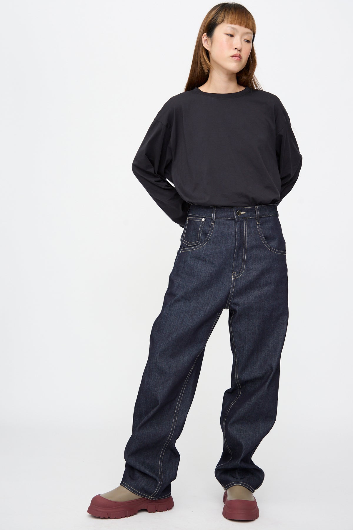 A person wearing a black long-sleeved shirt, Raw Denim Phill Pant in Midnight with contrast stitching, and brown shoes with red soles.