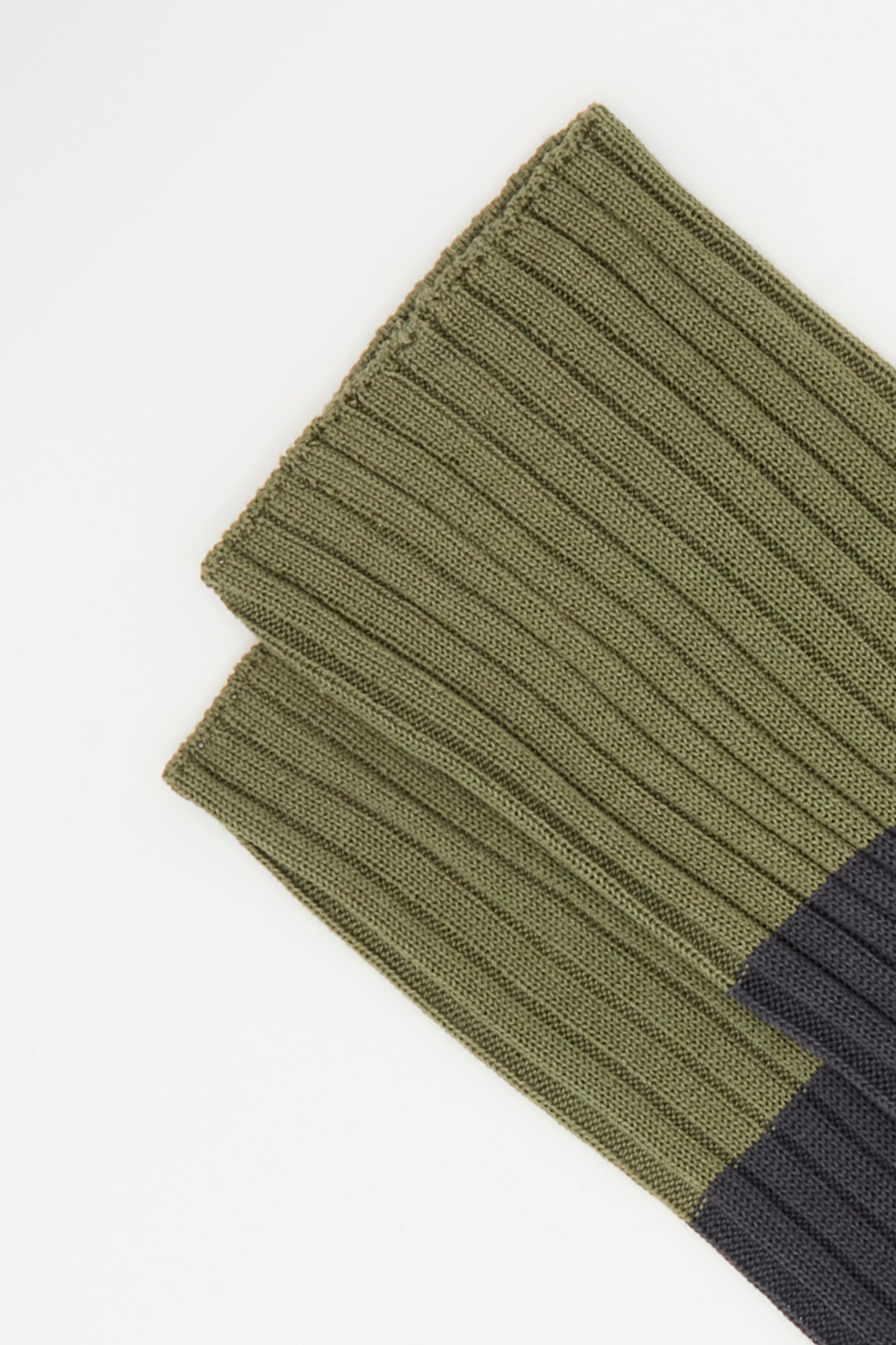 Close-up of Sofie D'Hoore's Rib Four Socks in Olive and Charcoal, featuring ribbed knit detailing that recalls the quality of Italian-made cotton socks. Laid on a white background, the olive green upper meets dark gray at the toe.