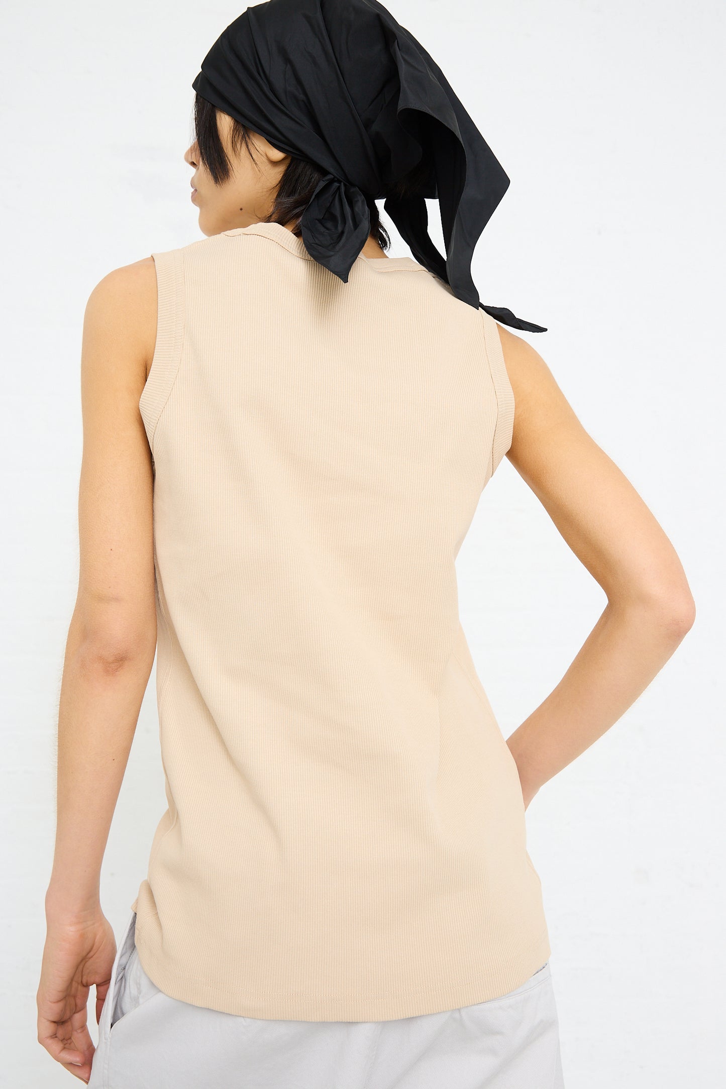 A person from behind wearing a beige Sofie D'Hoore rib knit tank in nude and a black headscarf.