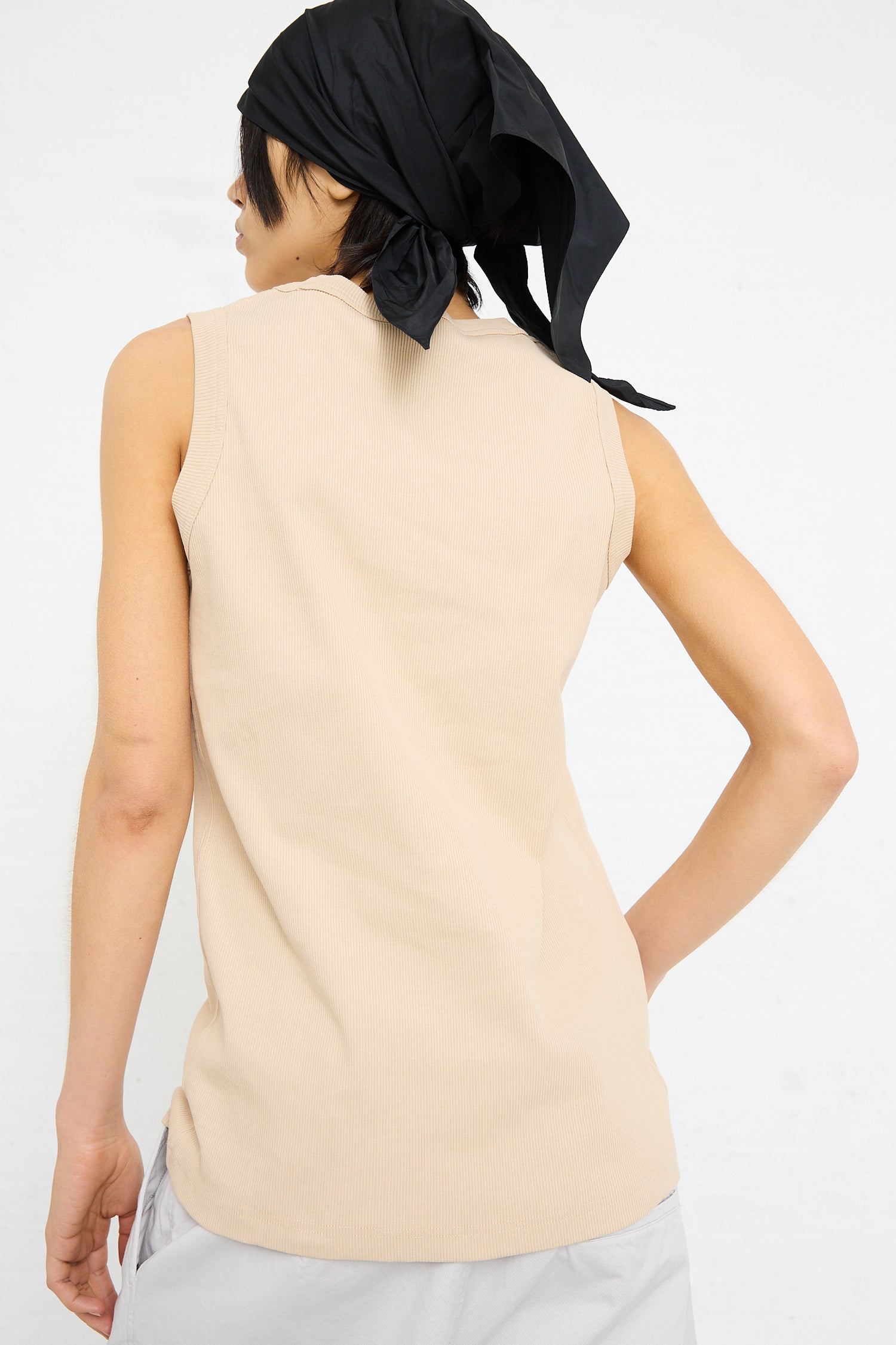 A person from behind wearing a beige Sofie D'Hoore rib knit tank in nude and a black headscarf.
