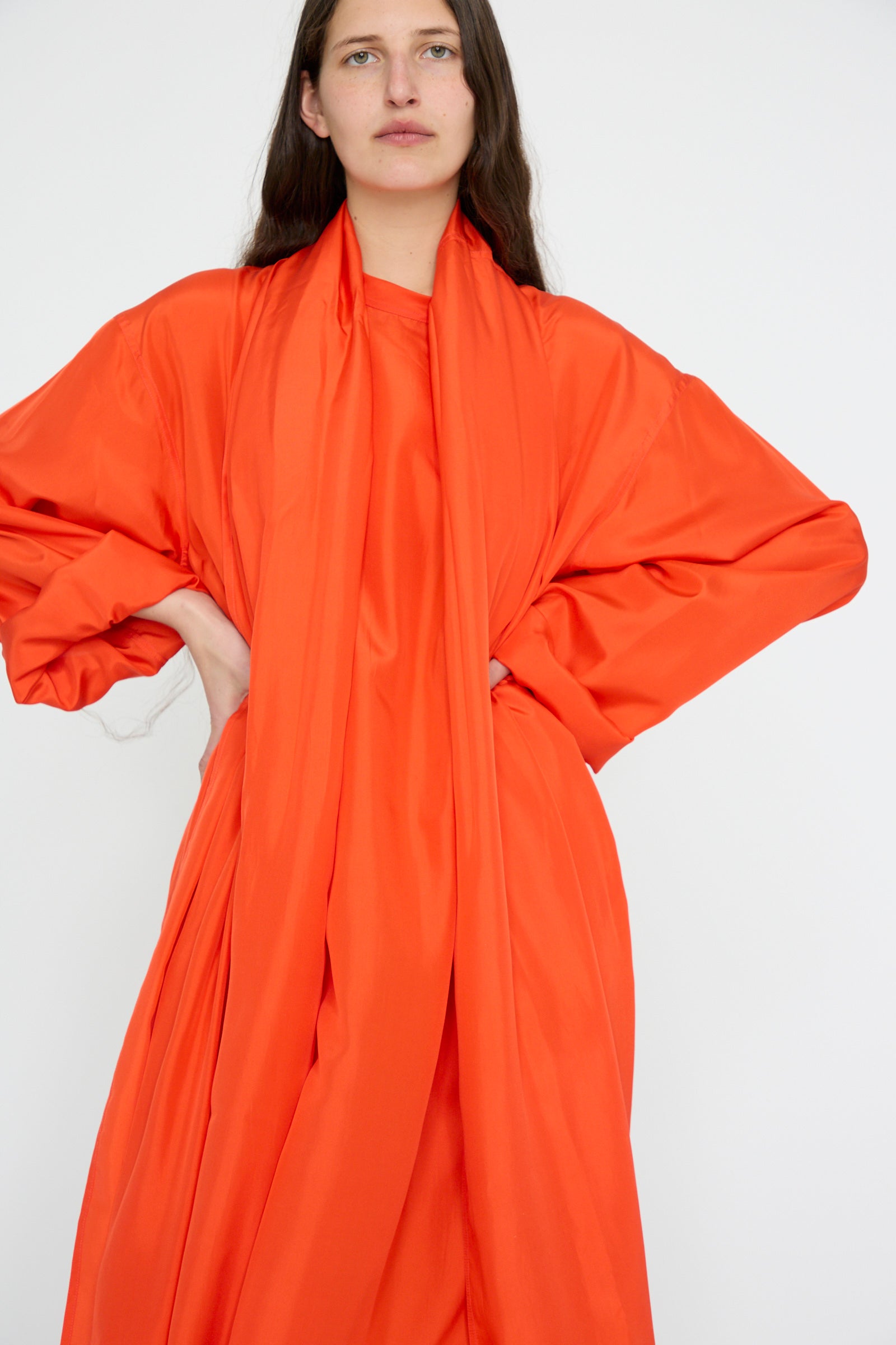 A person poses hands on hips, showcasing the Silk Habotai Dolphin Dress in Poppy by Sofie D'Hoore, against a white background.