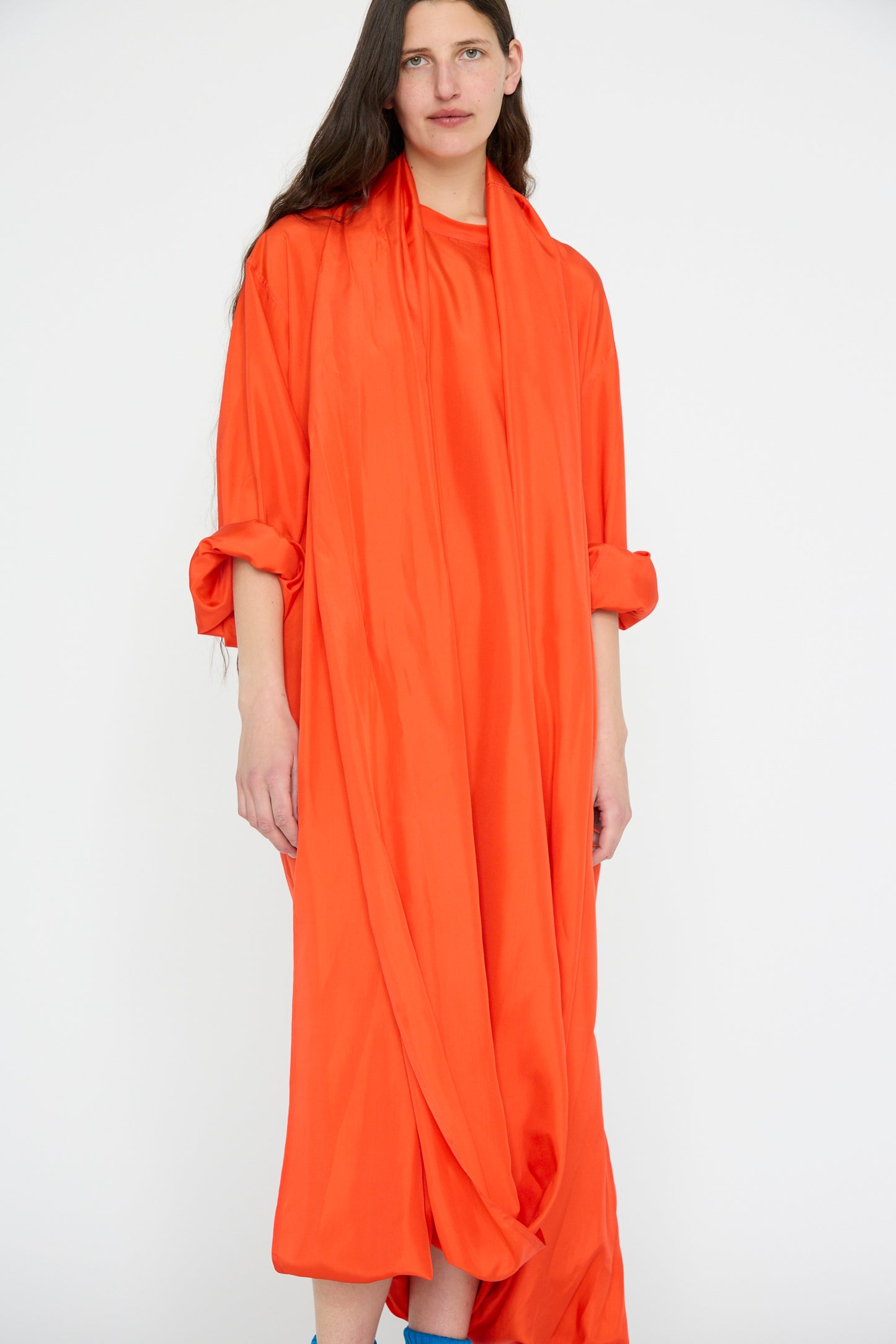 A person is dressed in a Silk Habotai Dolphin Dress in Poppy by Sofie D'Hoore, standing against a plain white background.