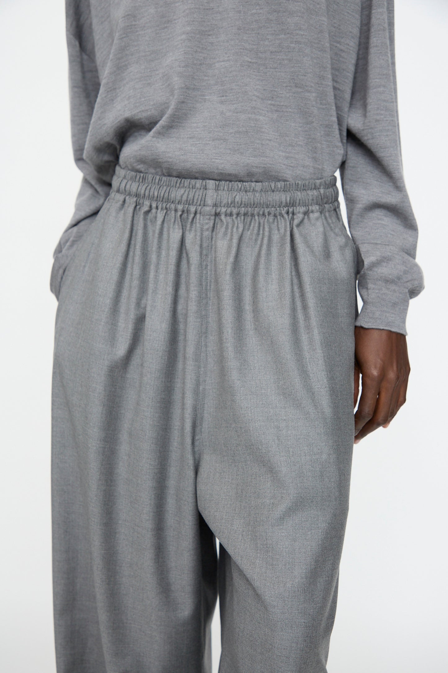 Person wearing Sofie D'Hoore Superfine Wool Pasch Pants in Mid Grey Melange, featuring a loose fit and elastic waistband, paired with a matching grey long-sleeve top. Shown from shoulders to knees.