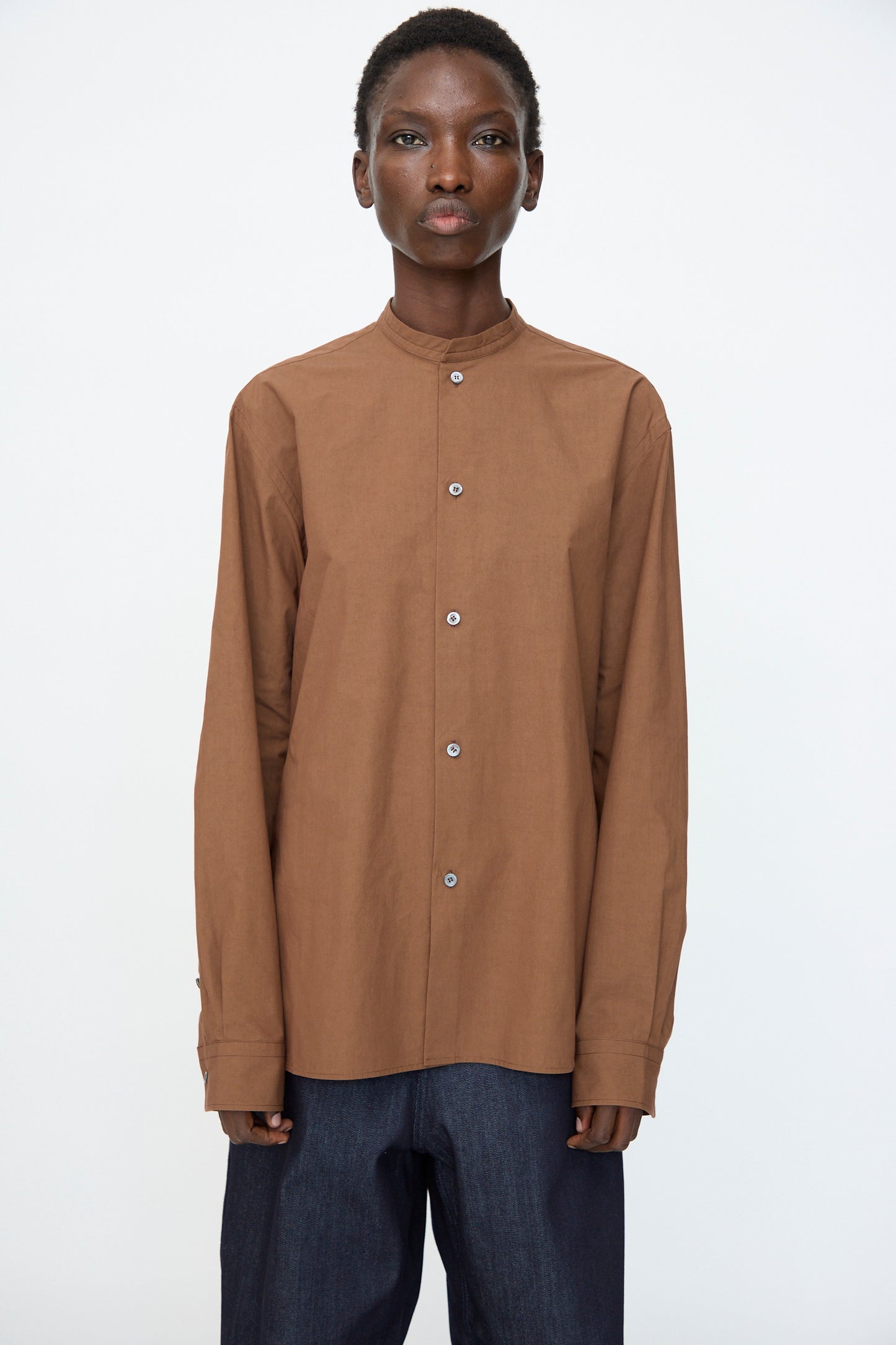 Model wears the Sofie D'Hoore Washed Poplin Braque Shirt in Chestnut with dark blue pants, standing against a plain white background.