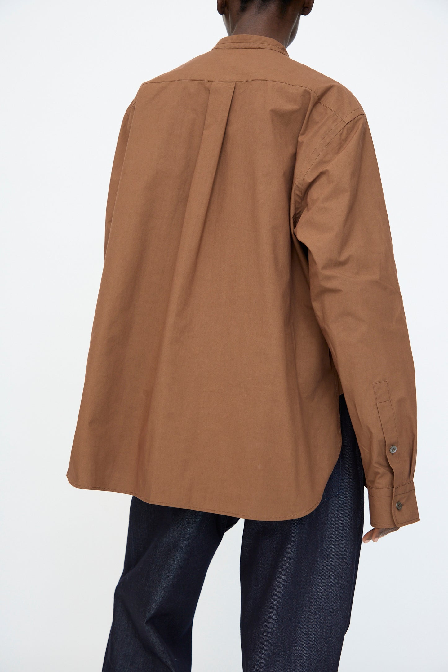Person facing away from the camera, wearing the Sofie D'Hoore Washed Poplin Braque Shirt in Chestnut and dark blue pants, set against a plain light background.