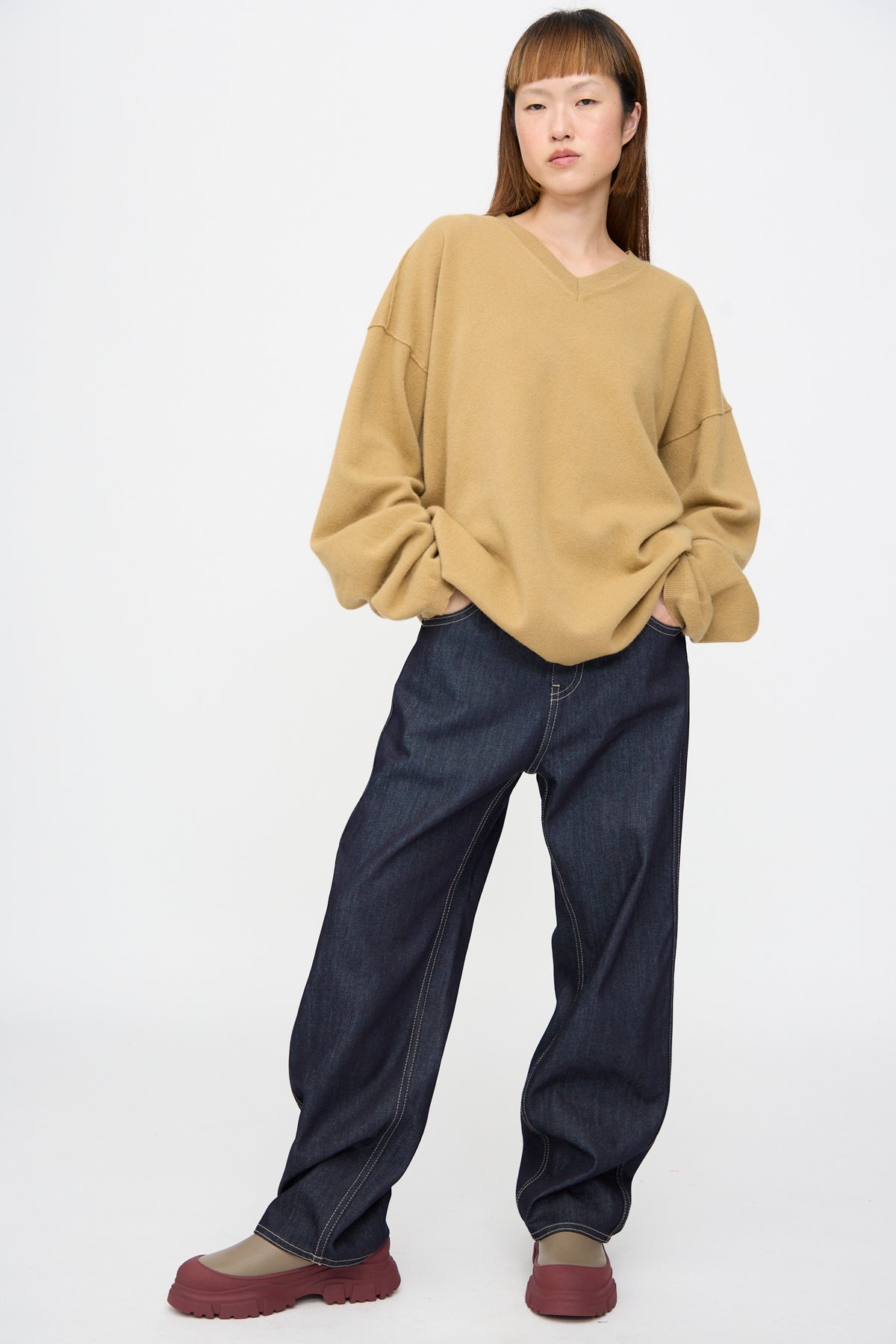 A model wearing a camel Wool Maurice Sweater with oversized sleeves, dark blue wide-leg jeans, and maroon lug-sole shoes.
