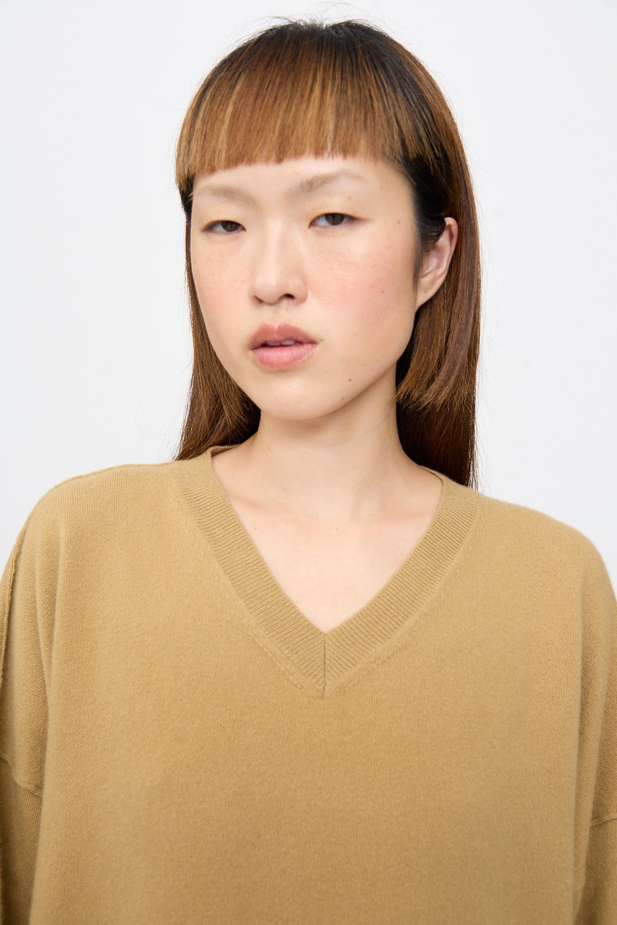 A person wearing an oversized, camel-colored Wool Maurice Sweater in Camel with a V-neck.