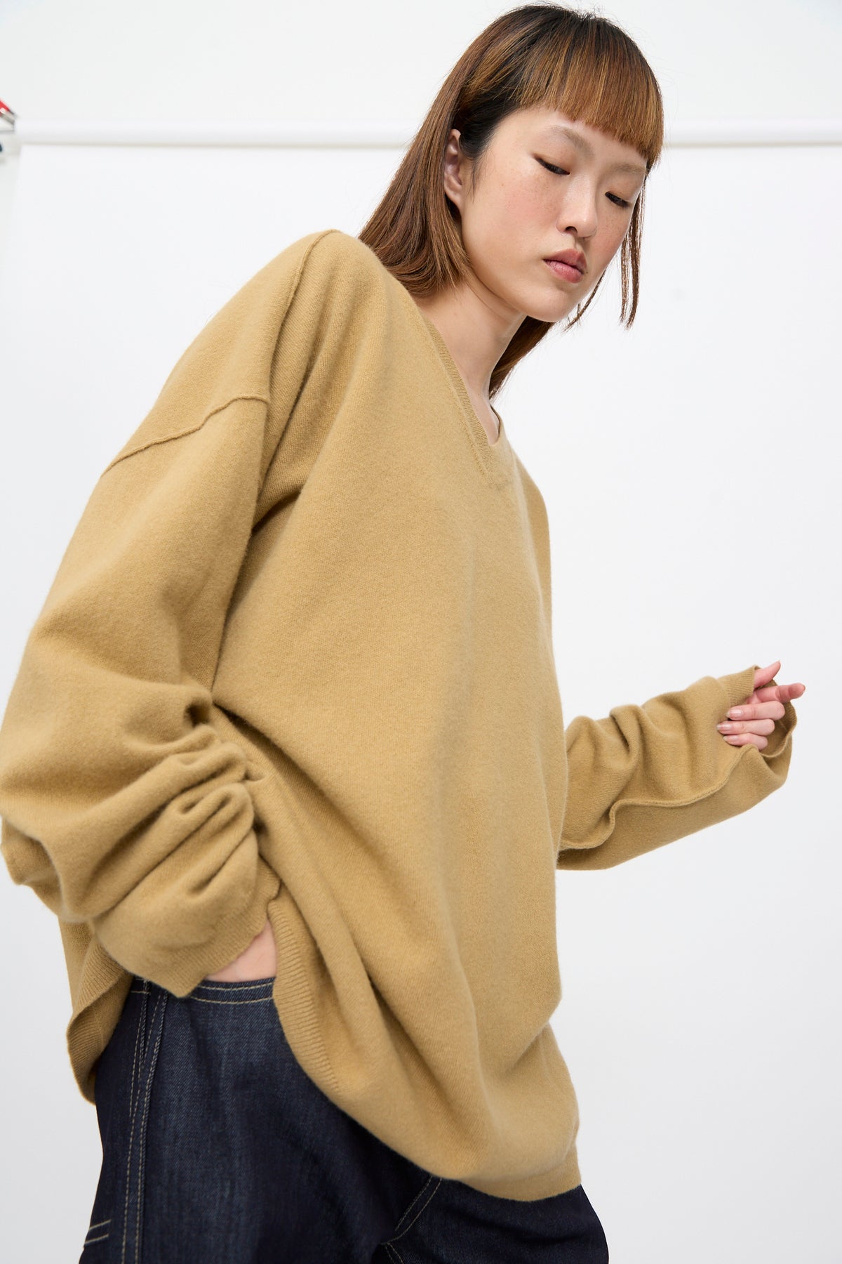 A person wearing an oversized camel-colored Wool Maurice Sweater with long sleeves and dark jeans.