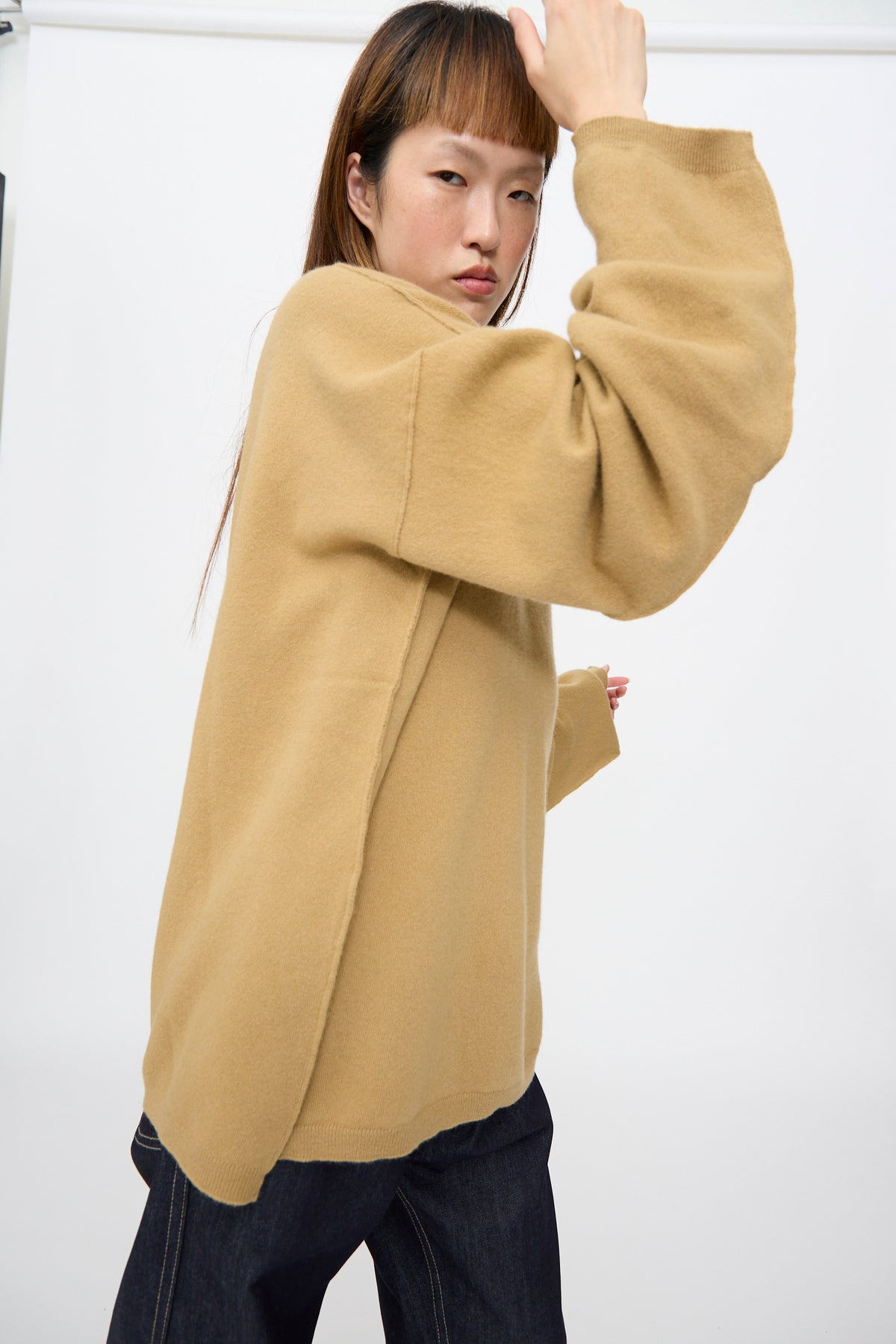 A person wearing an oversized, camel-colored Wool Maurice Sweater in Camel with a V-neck and dark jeans.