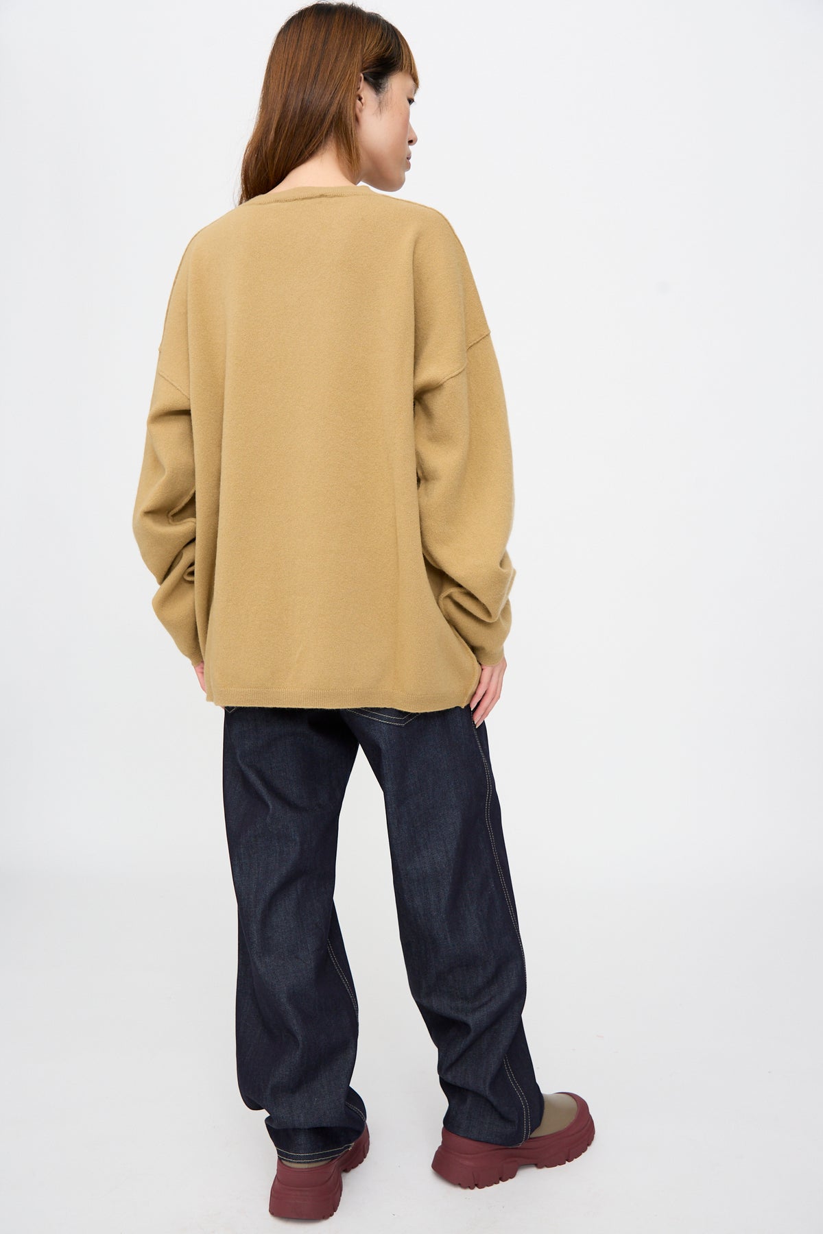 Person seen from behind wearing an oversized camel-colored Wool Maurice Sweater in Camel V-neck, dark blue wide-leg jeans, and platform boots.