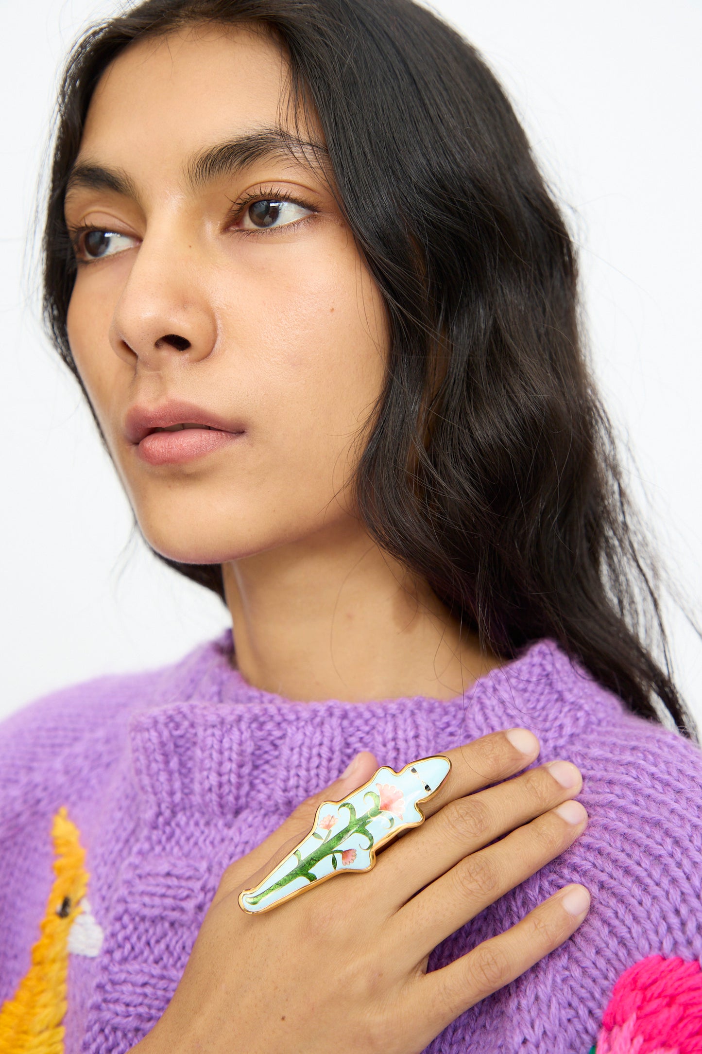 A person with long dark hair wearing a purple sweater and the Sofio Gongli Alligator Ring in Blue poses against a plain light background.
