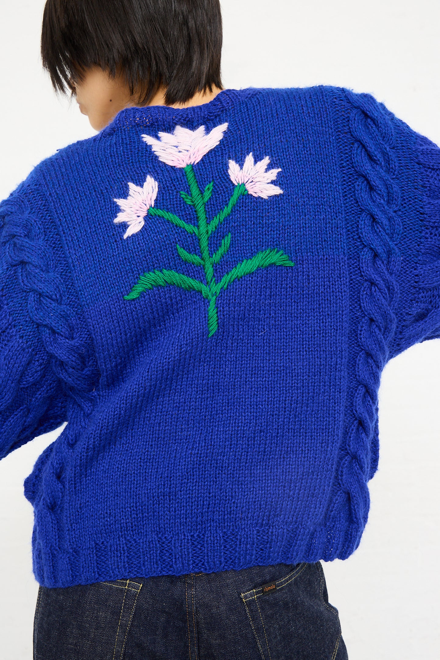 A person from behind wearing a Sofio Gongli Animal Floral Sweater in Blue with cable knit details on the sleeves.