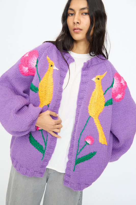 A person wears the Sofio Gongli "Cardigan in Purple with Bird and Flower" over a white shirt and gray pants.