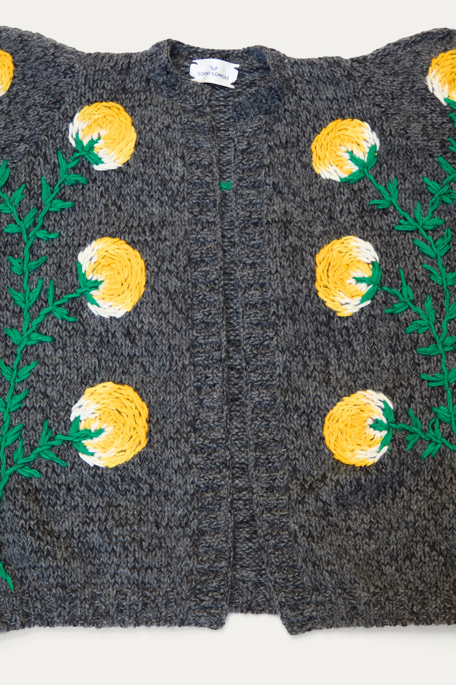 The Sofio Gongli Cardigan with Yellow Flower in Grey features a mohair wool blend and is adorned with an embroidered design of yellow and white floral patterns accented by green leaves against a white backdrop. 