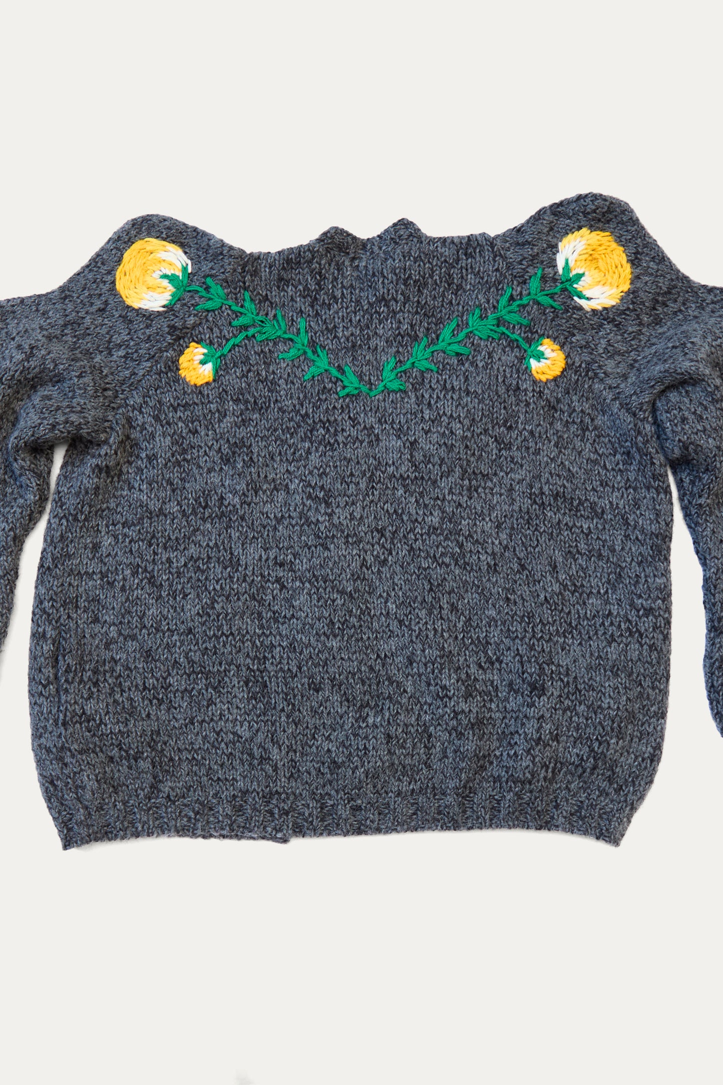 The Sofio Gongli "Cardigan with Yellow Flower in Grey" is a hand-knit gray sweater made from a soft mohair wool blend, showcasing a yellow and green embroidered design on the front.