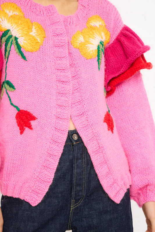 Close-up of a woman wearing a Sofio Gongli pink, hand-knit Floral Sweater with floral embroidery, paired with denim jeans. Only the torso is visible.