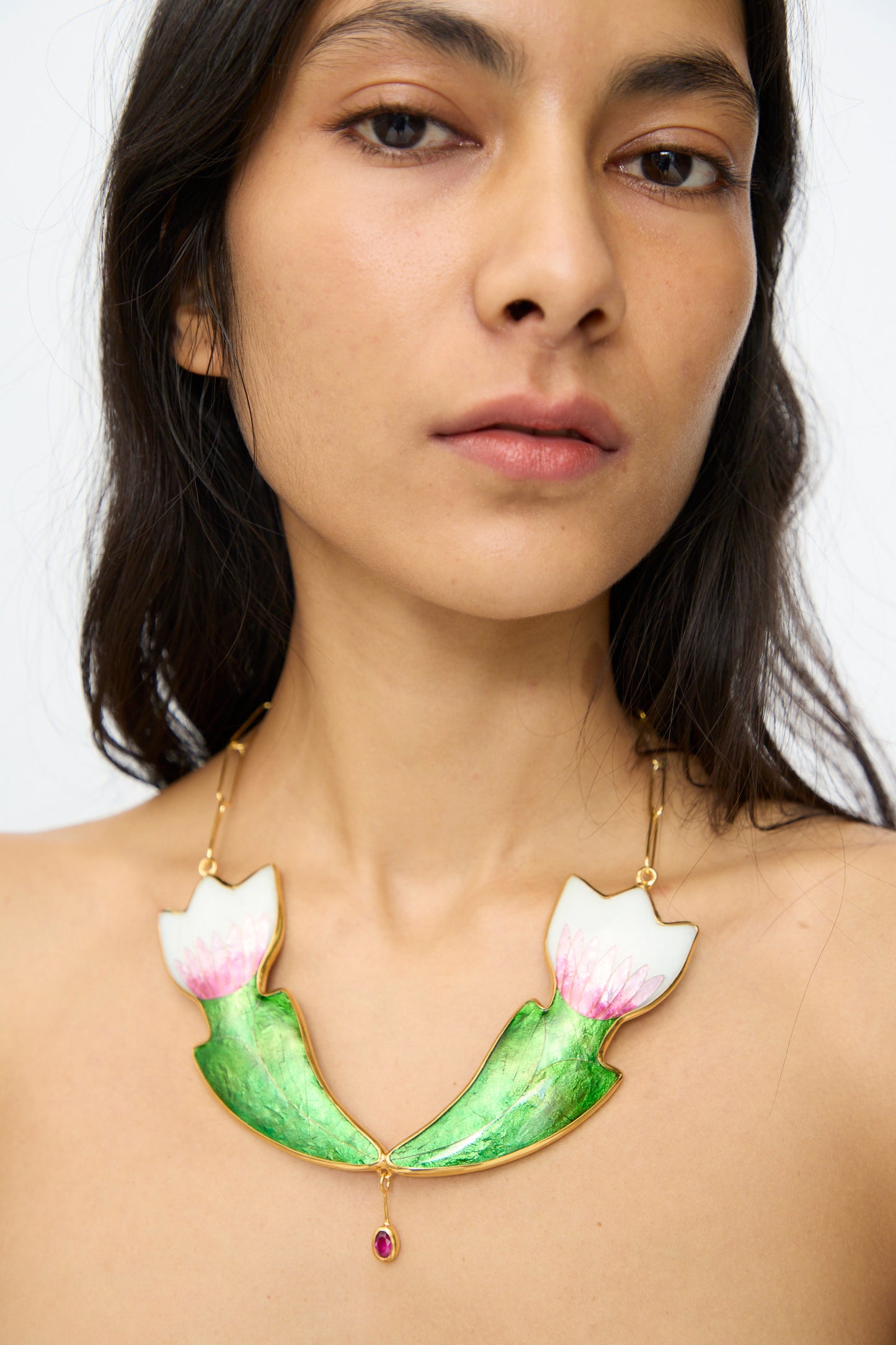 A woman wearing the Sofio Gongli Flower Necklace—14k gold plated, featuring two pink and white enamel flowers, green leaves, and a small dangling pendant.