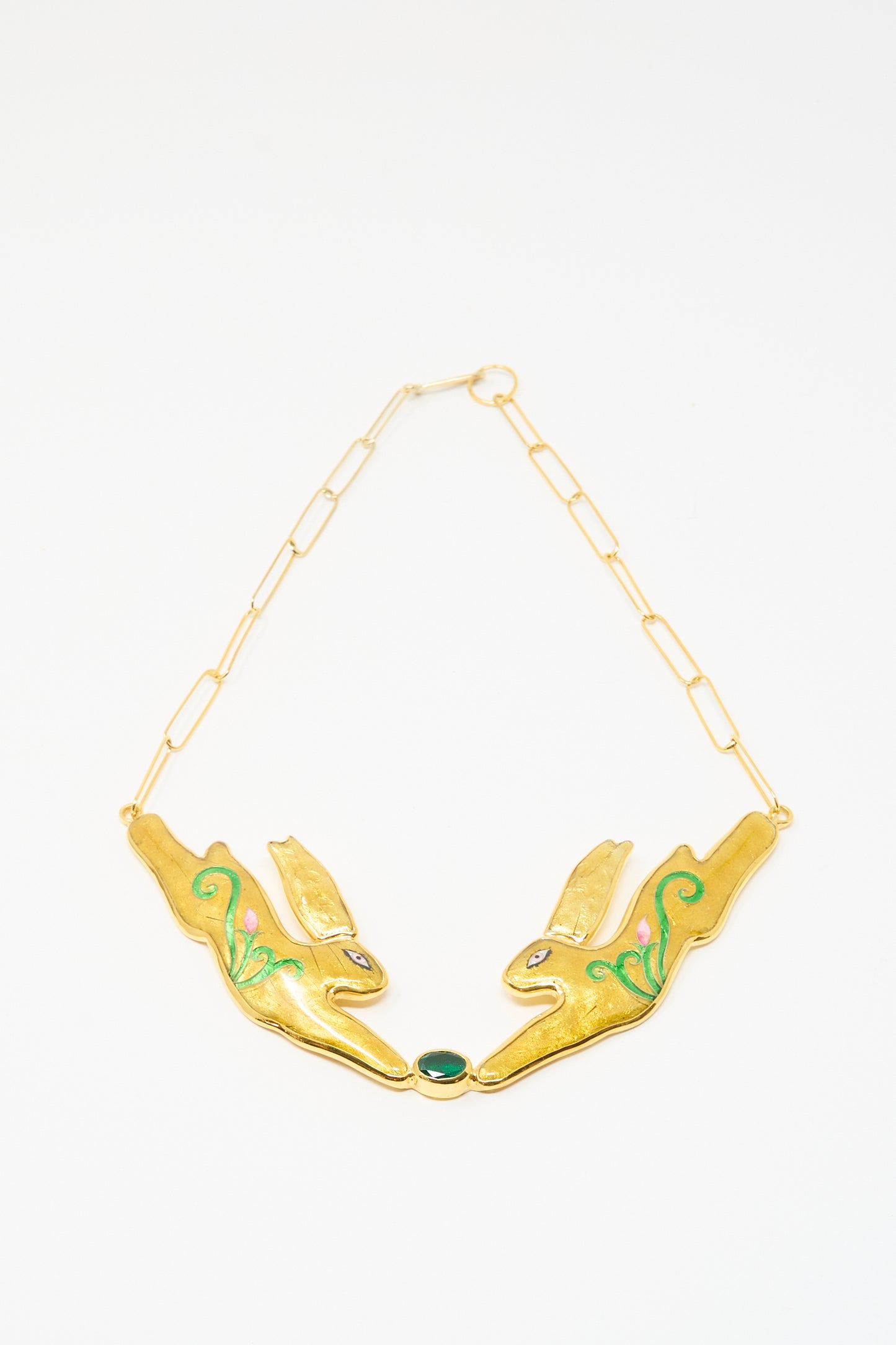 The Hare Necklace by Sofio Gongli showcases two stylized rabbit heads with green details, linked by a chain and a central green oval stone, echoing the look of Byzantine cloisonné jewelry.