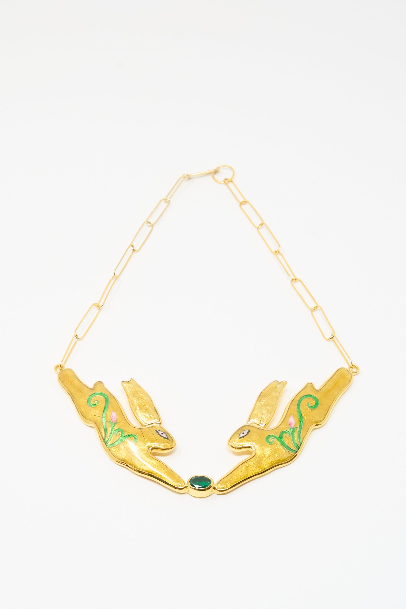 The Hare Necklace by Sofio Gongli showcases two stylized rabbit heads with green details, linked by a chain and a central green oval stone, echoing the look of Byzantine cloisonné jewelry.