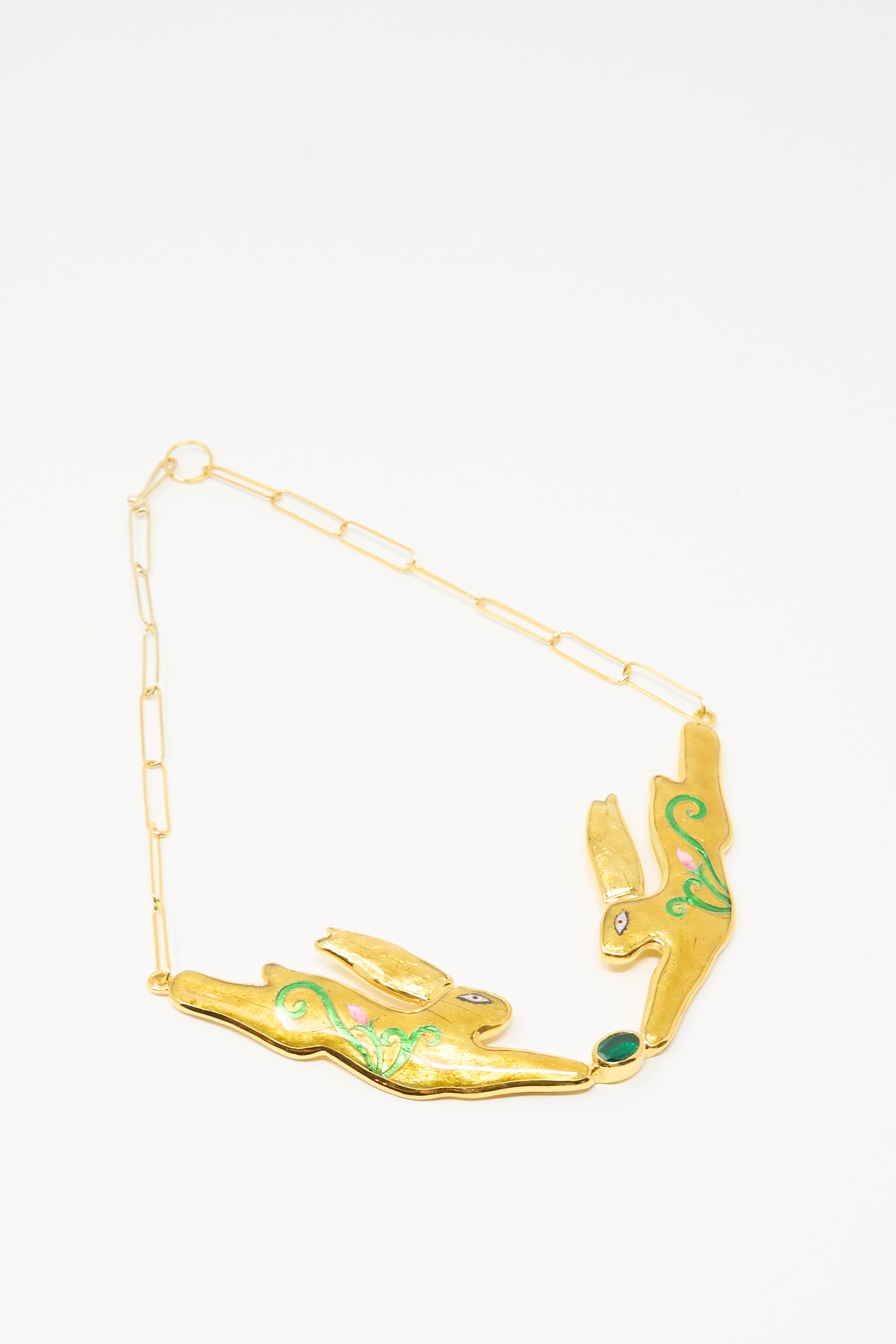 The Sofio Gongli Hare Necklace is a 14K gold plated piece featuring two stylized hare figures with green enamel and gemstone accents, linked by a delicate chain inspired by Byzantine cloisonné design.