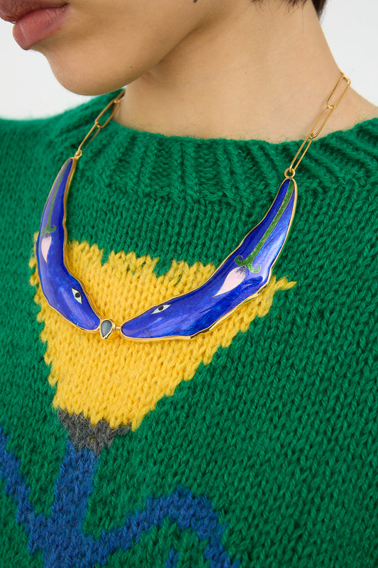A person wearing a green and yellow knitted sweater with a blue, cloisonné enamel Sofio Gongli Banana-Shaped Necklace in Blue Animal.