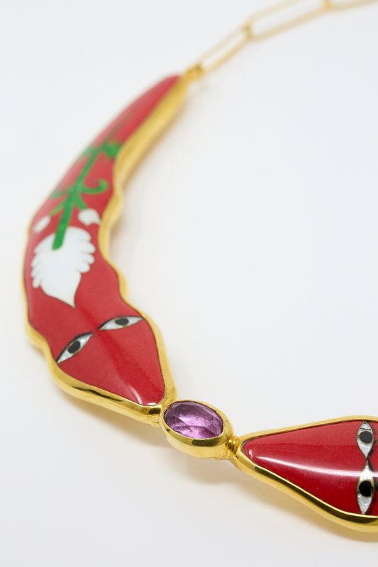 A close-up view of a section of a Sofio Gongli decorative necklace displaying the cloisonné technique with red enamel and a central purple gemstone set in a gold-tone metal on a white background.