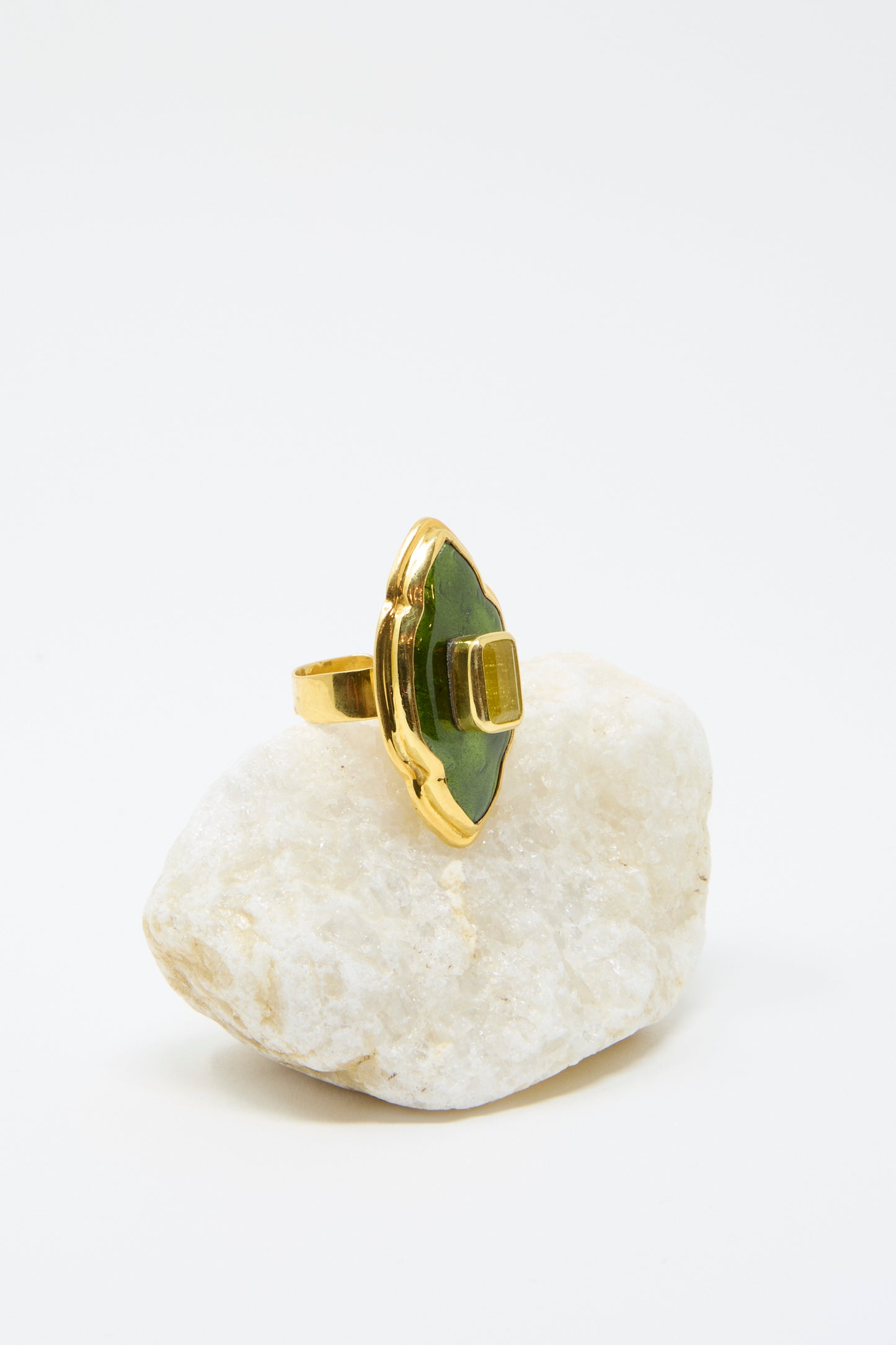 Sofio Gongli's "Ring in Green and Gold" features a striking Byzantine cloisonné design with a gold band and vivid green gemstone, displayed on a textured white stone against a plain background.