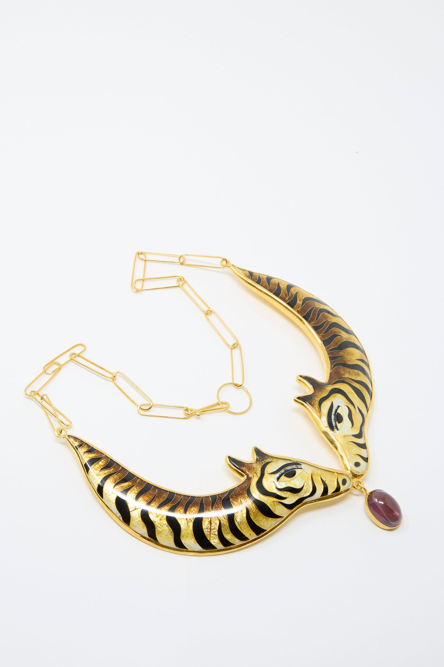 The Striped Animal Necklace by Sofio Gongli features a gold cloisonné design with two stylized animal heads, accented by striped enamel and a prominent red corundum stone at its center.