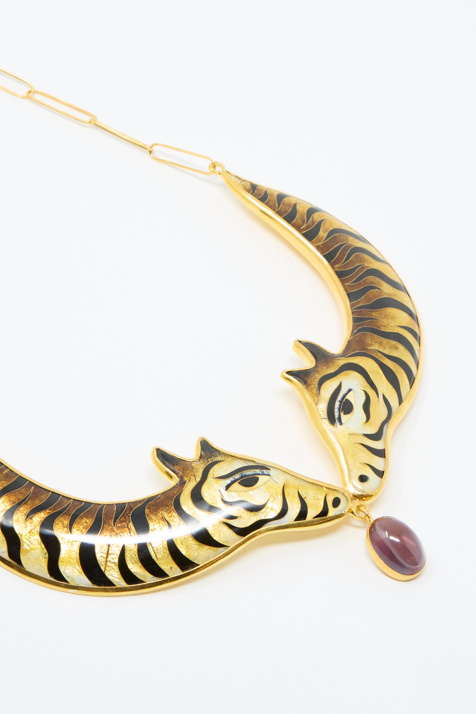 The Striped Animal Necklace by Sofio Gongli features a 14K gold plated silver design with two black-striped animal heads, centered around a stunning purple corundum stone against a white backdrop. 