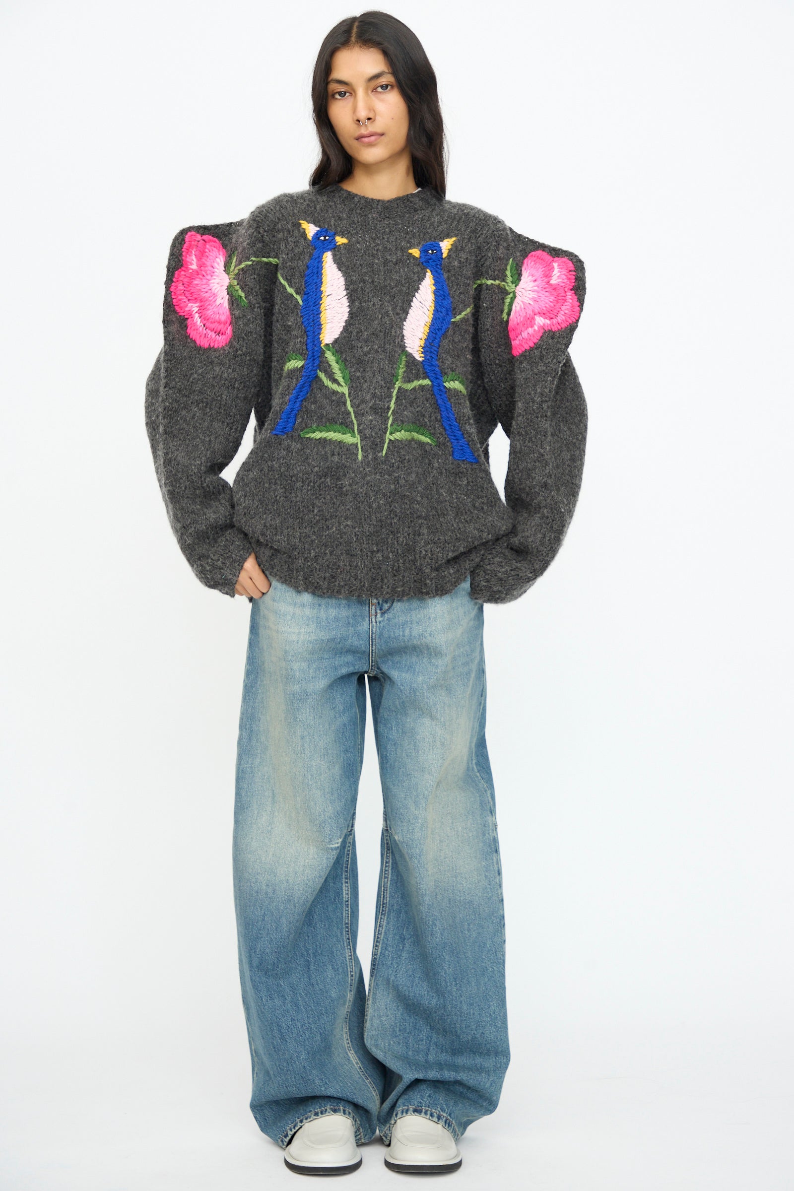 A woman faces forward wearing the Sofio Gongli Sweater in Charcoal with Birds and Flowers, paired with wide-leg jeans and white sneakers, standing against a plain white background.