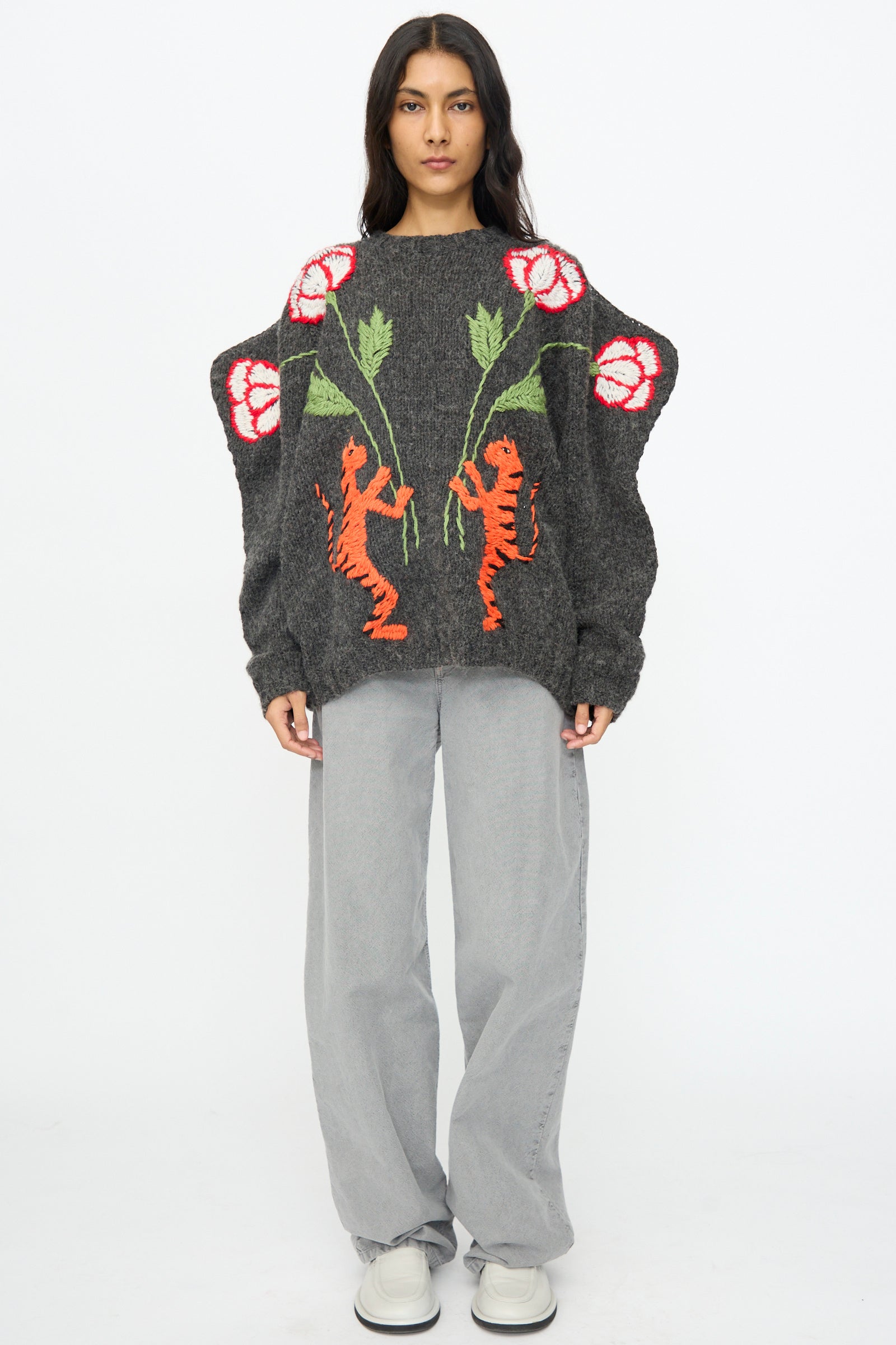 A person stands facing forward wearing a Sofio Gongli charcoal sweater with tiger and flower motifs, light gray loose pants, and white shoes against a plain white background.